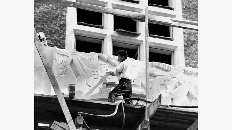 An artist on scaffolding carving on the facade of the MSU Union building