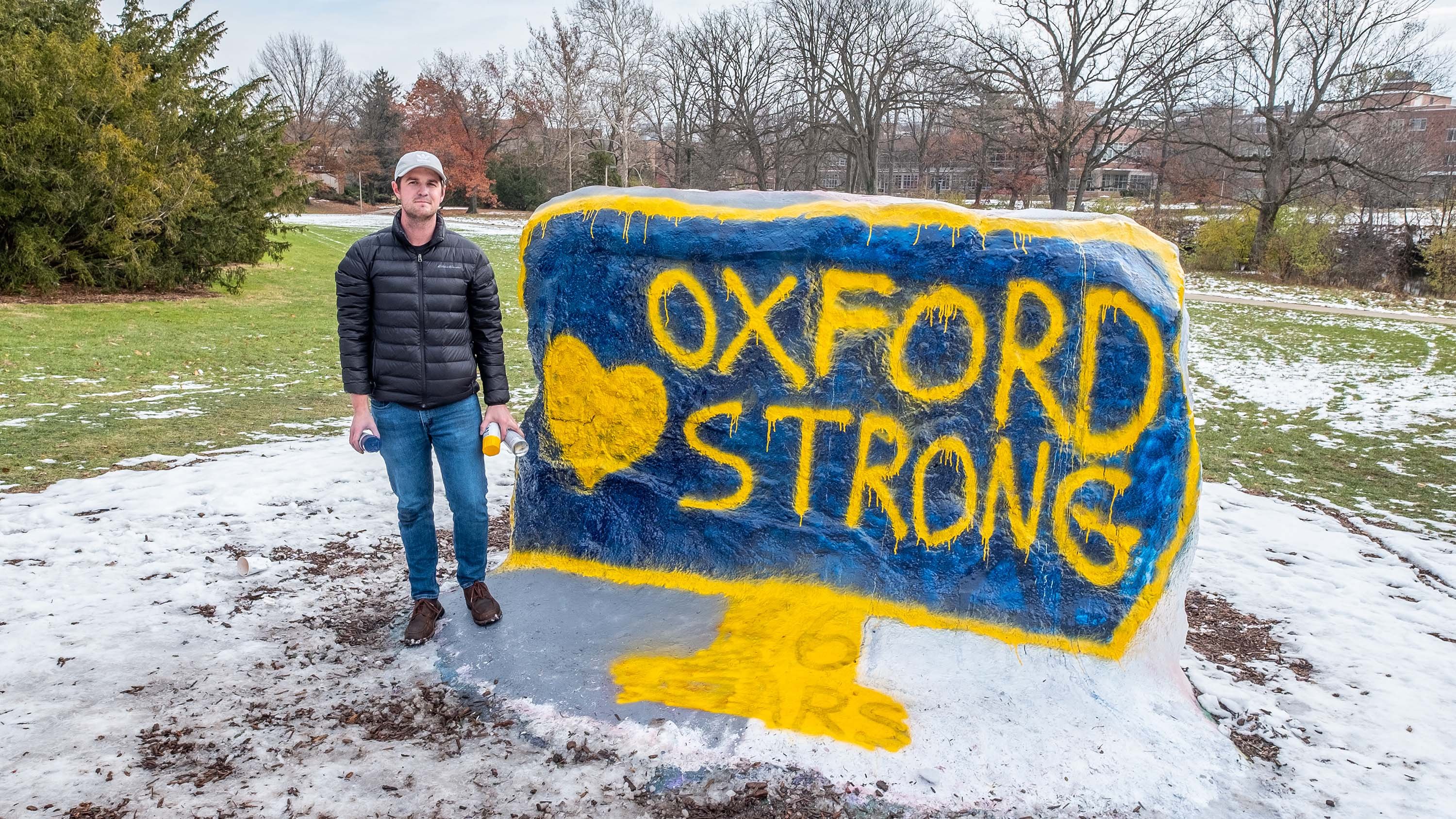 MSU student Brendan Ruehl stands next to the MSU Rock, which is painted in blue and yellow with the phrase 'Oxford Strong'