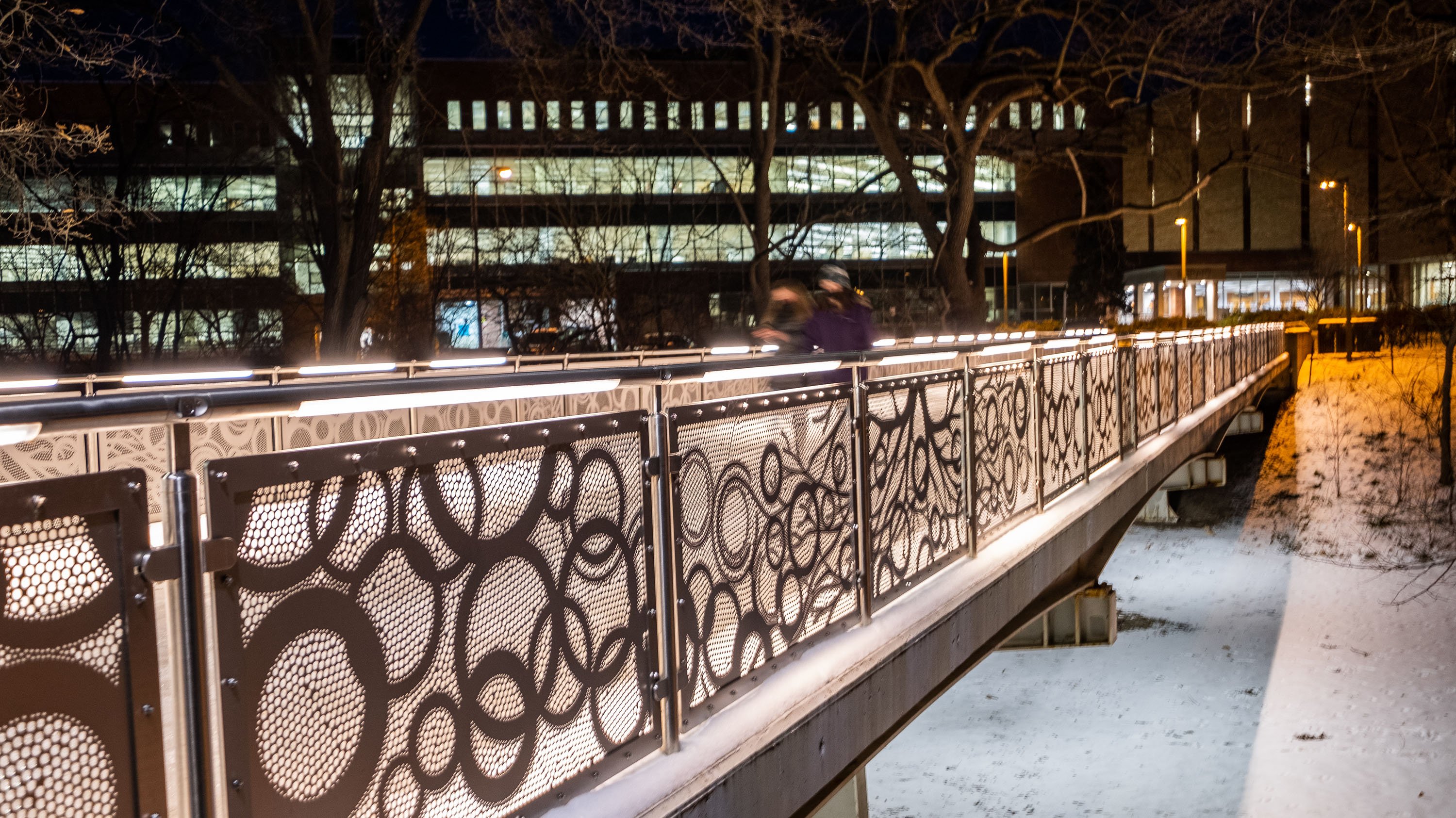 Students cross the library bridge at night