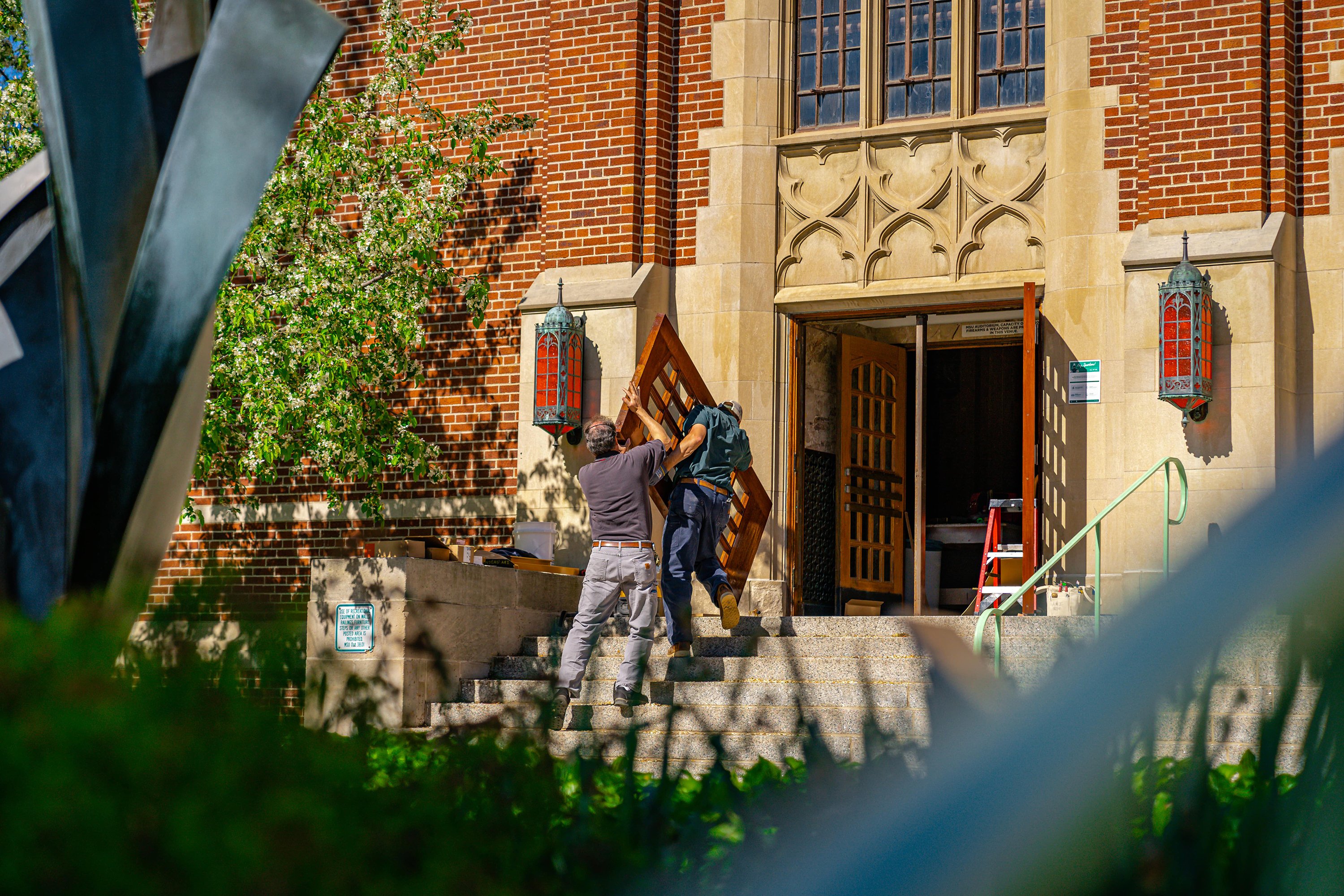 two men carrying a door through doorway to MSU Aud