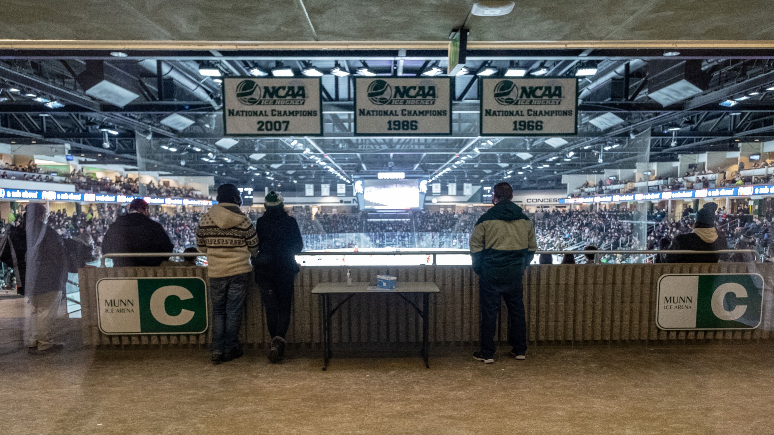Spectators watching hockey game in Munn Ice arena, seen from behind