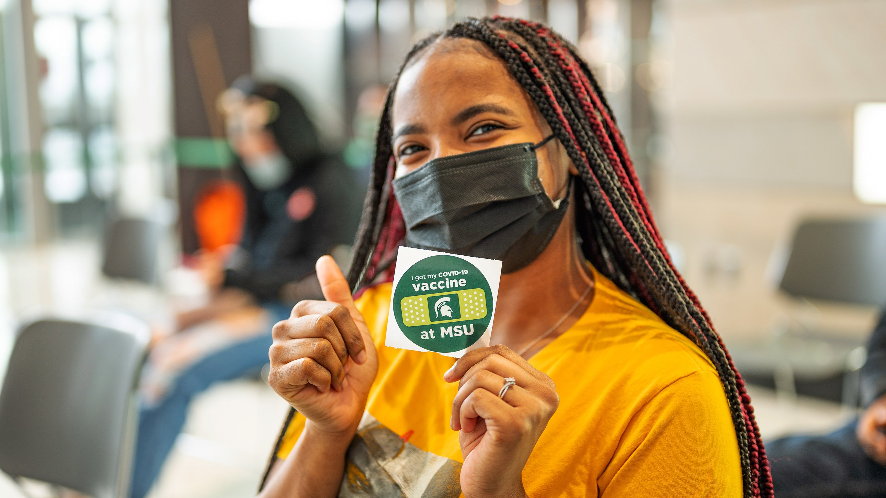 Student holding up a sticker that reads 'I got my Covid-19 vaccine at MSU'