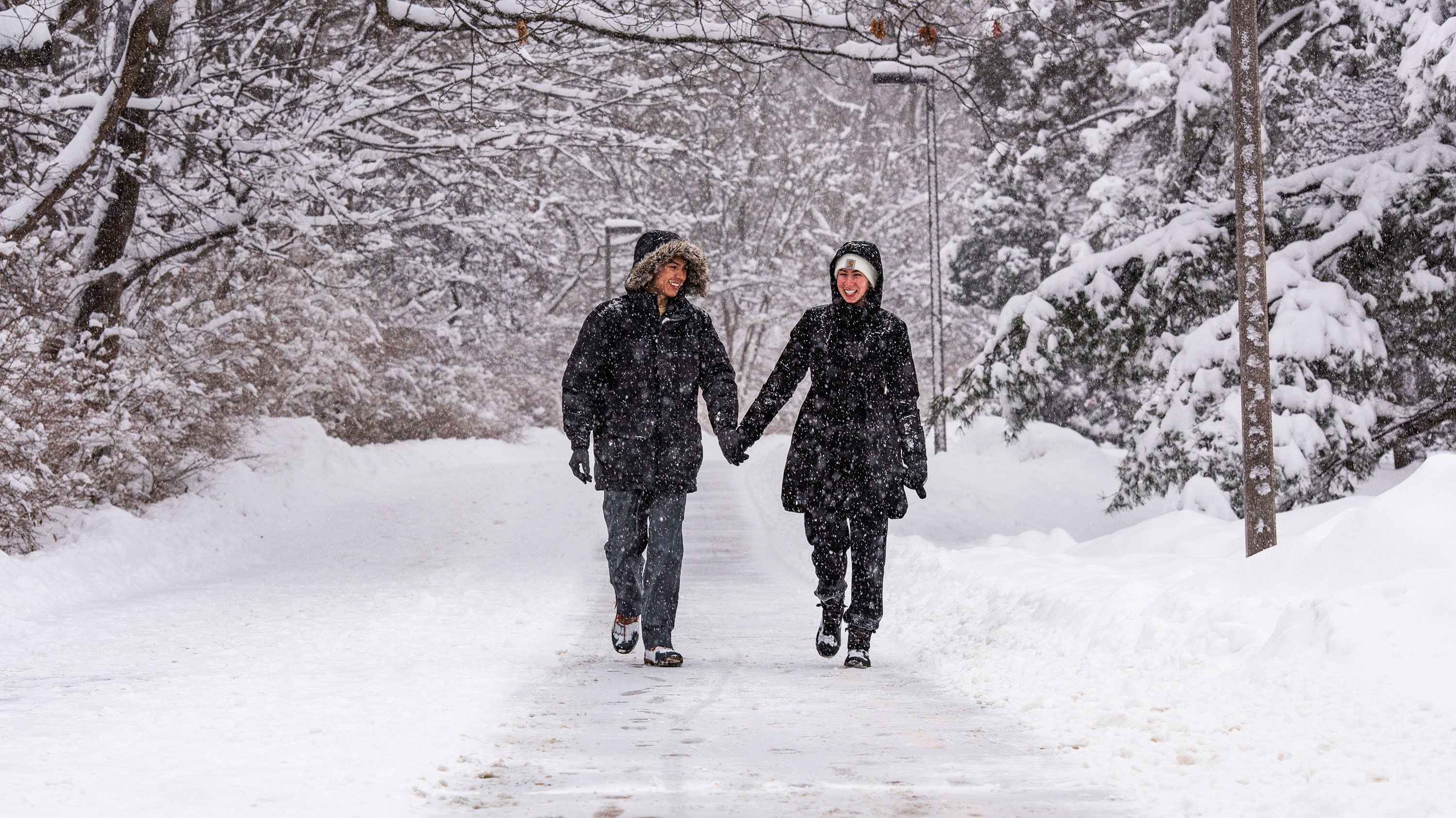 Two people walking and holding hands on campus in a winter storm