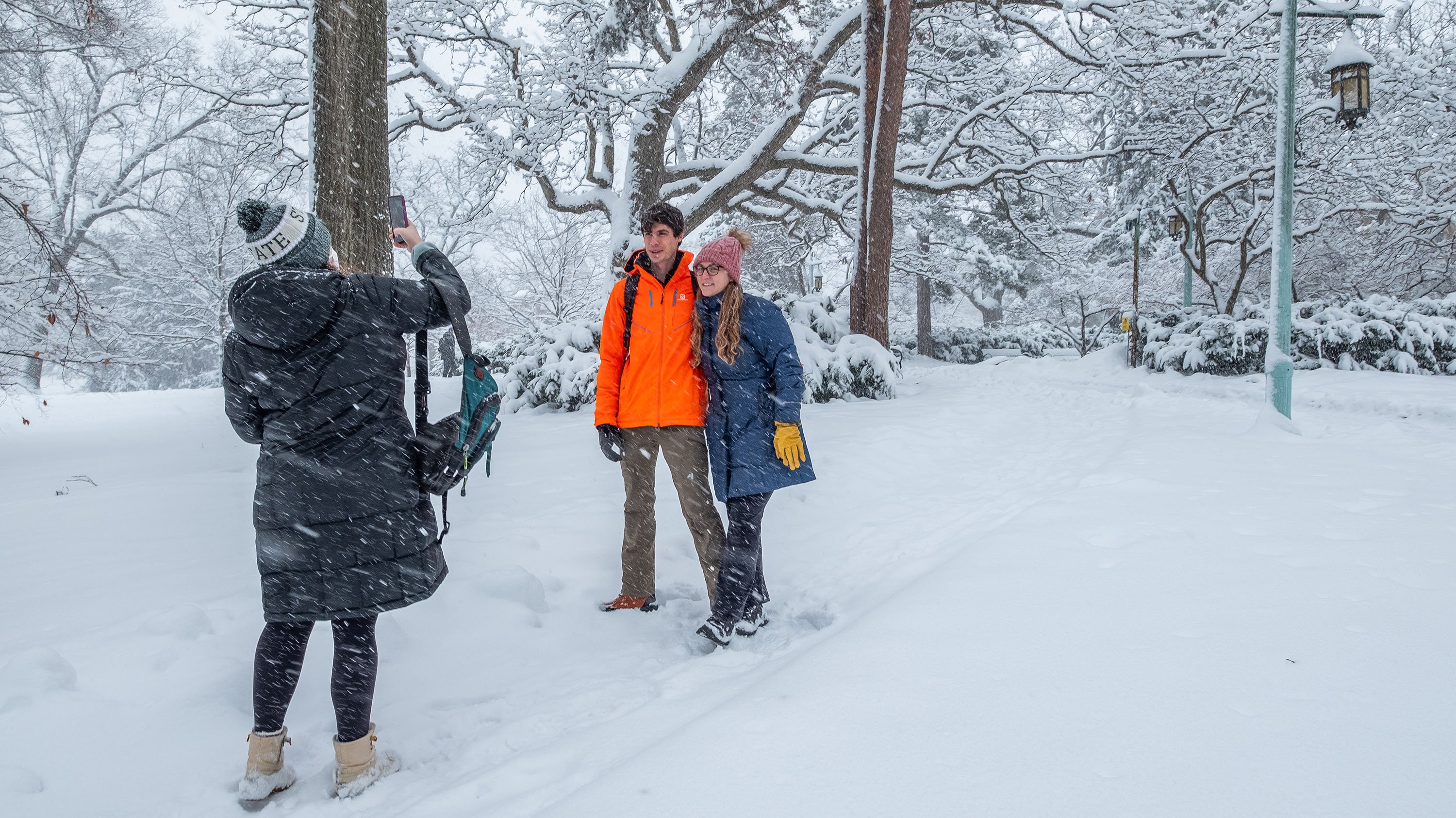Person taking picture of two others on campus during winter snowfall