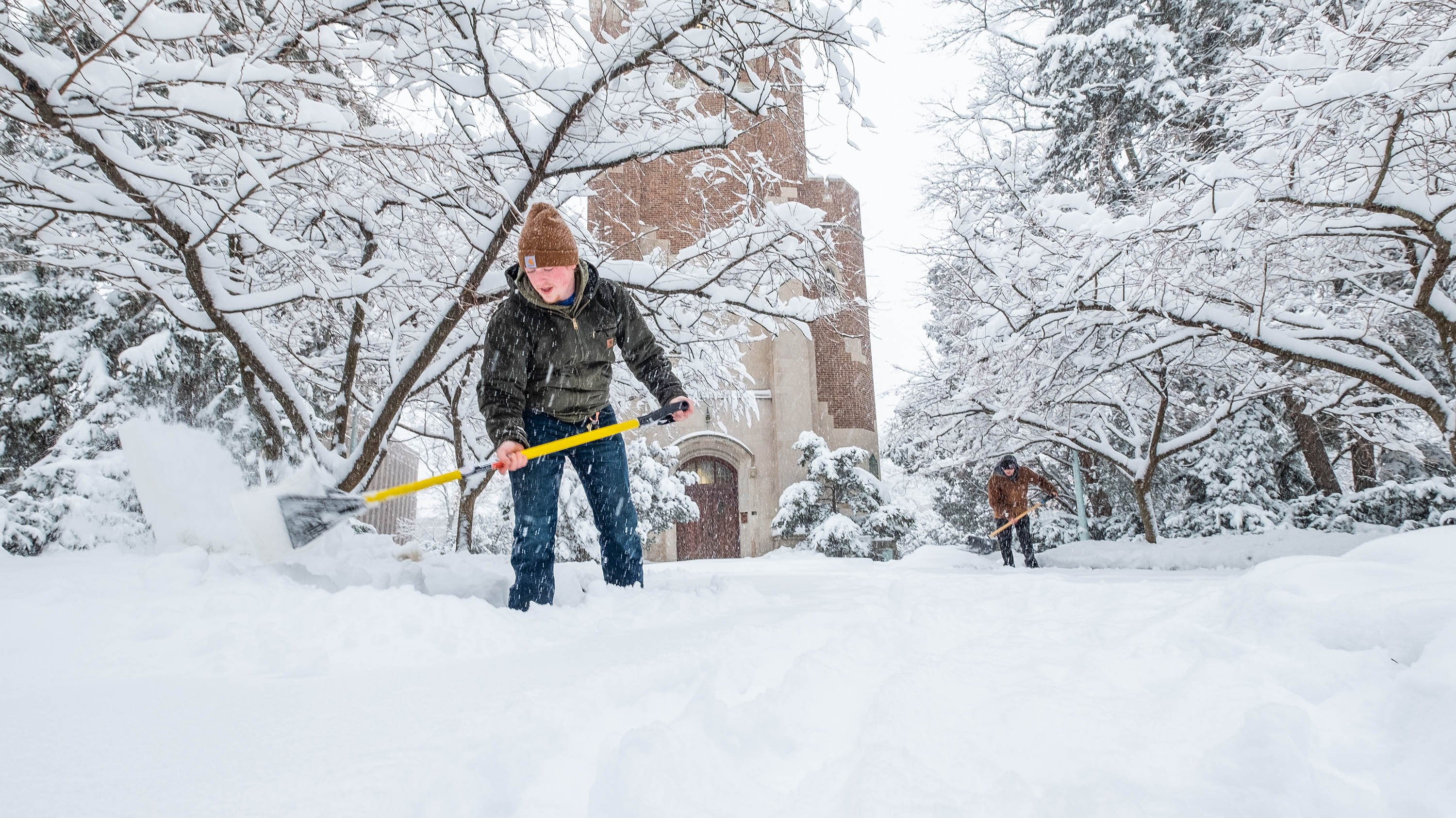 Two IPF employees shoveling snow in front of Beaumont Tower