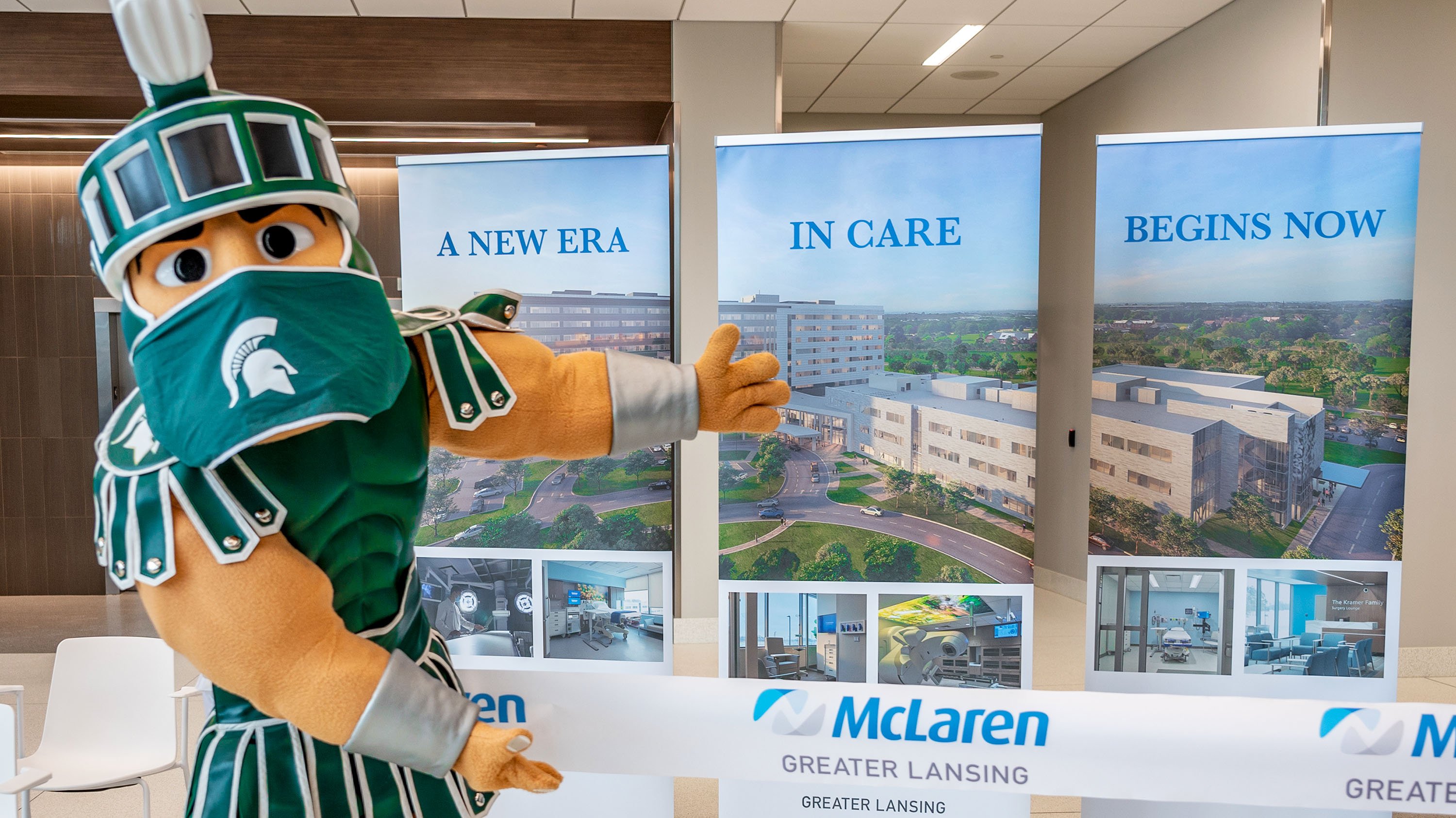 Sparty standing in front of signs at the McLaren Greater Lansing Health Care Campus, which read 'a new era in care begins now'
