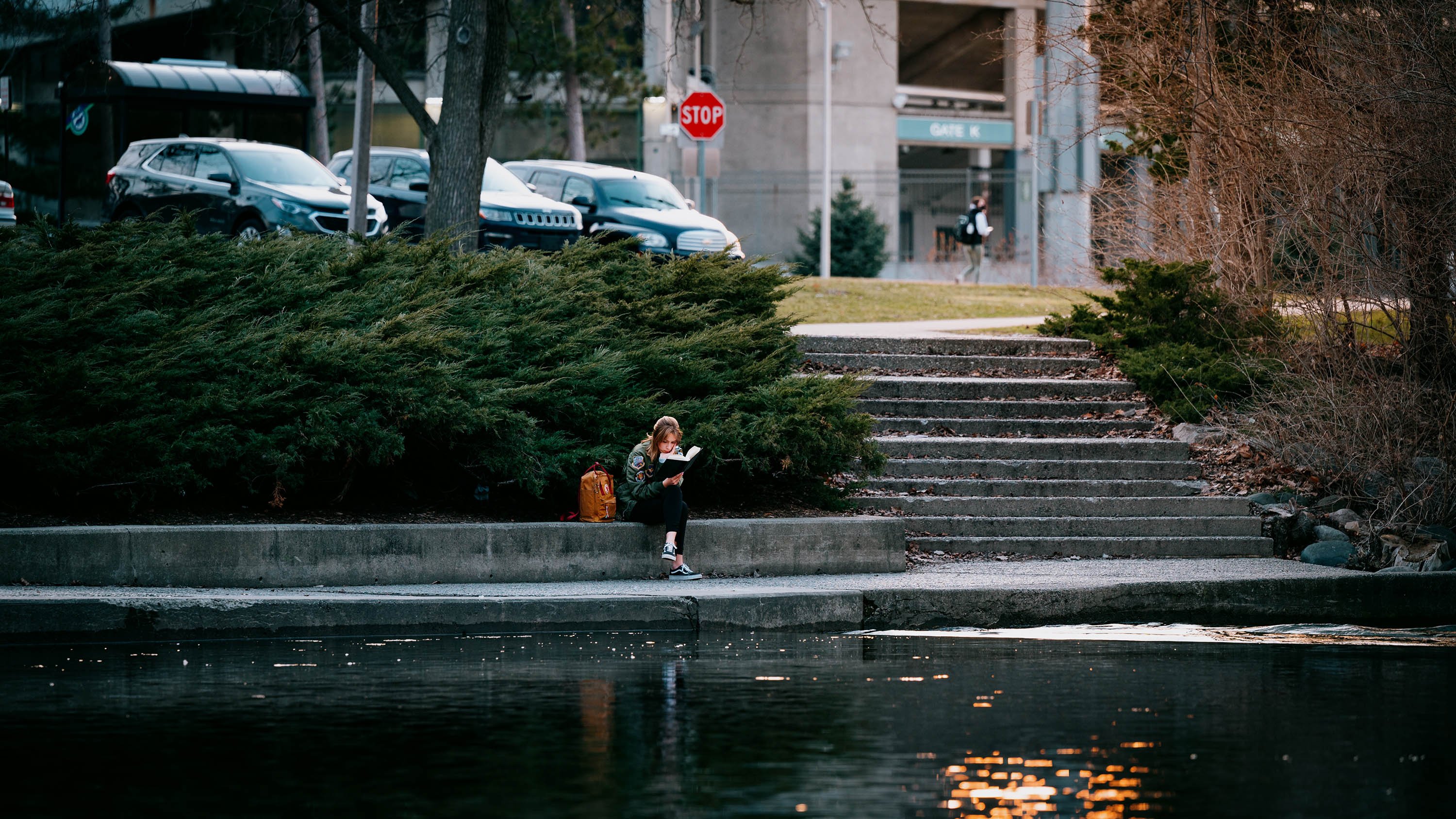 Student sitting on bank of Red Cedar river holding a book