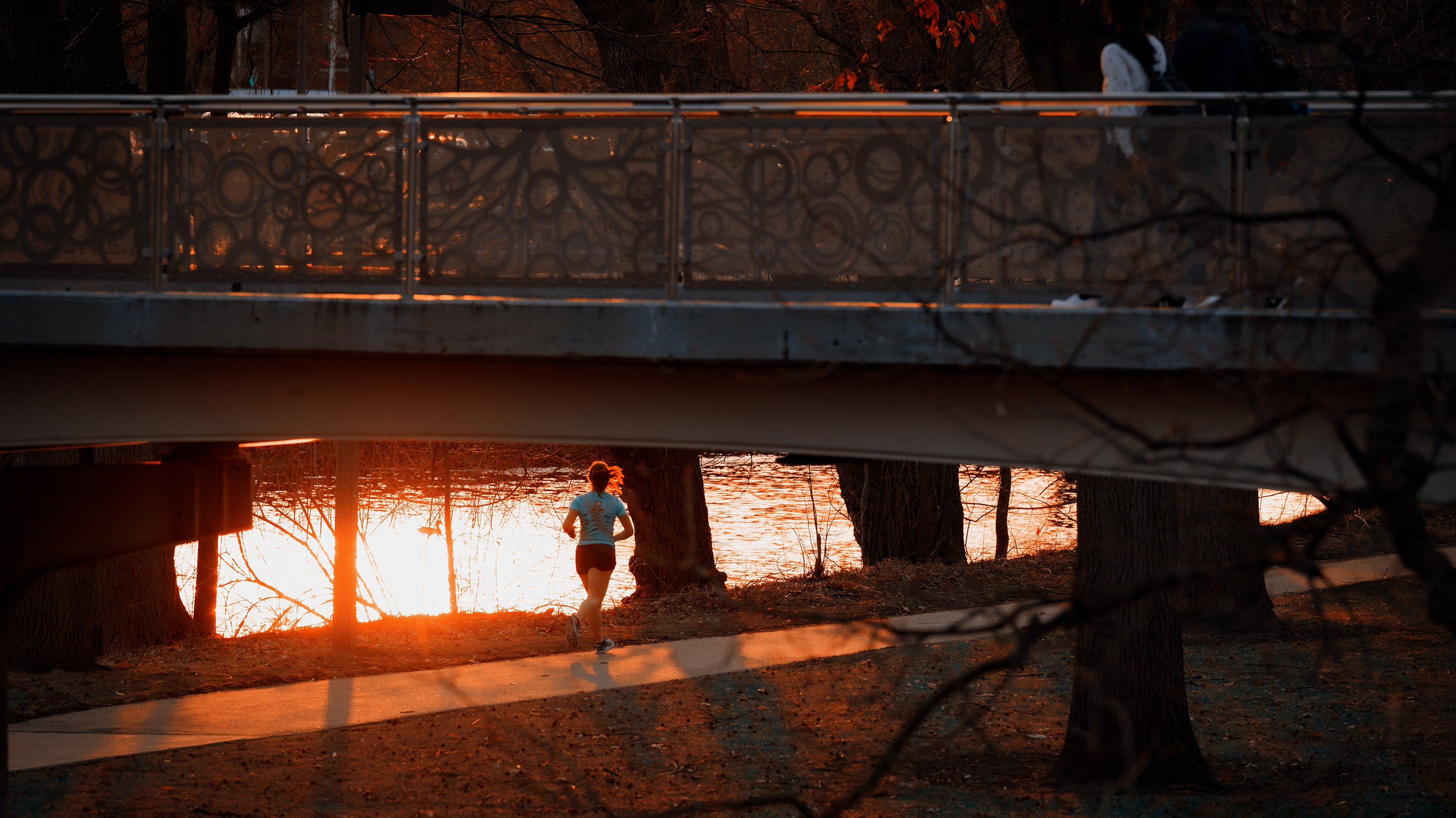 Person running next to Red Cedar river at sunset
