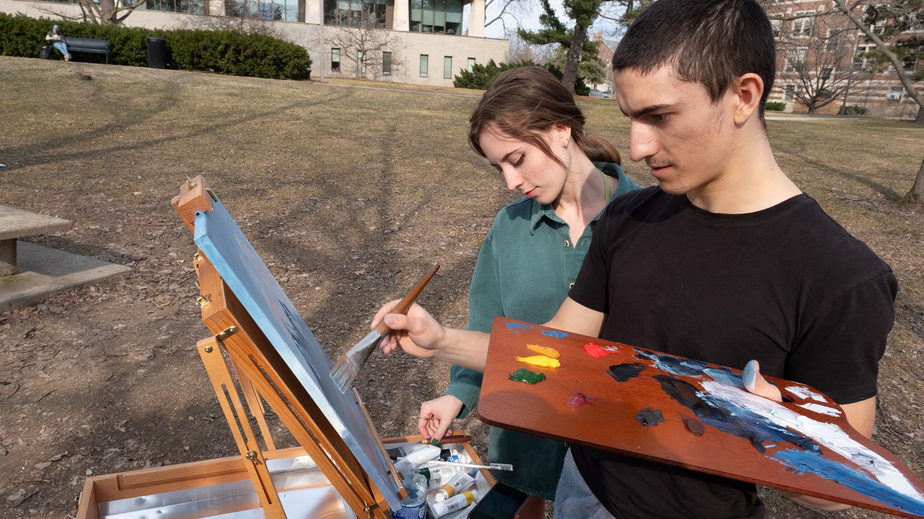 Two people painting outside on an easel