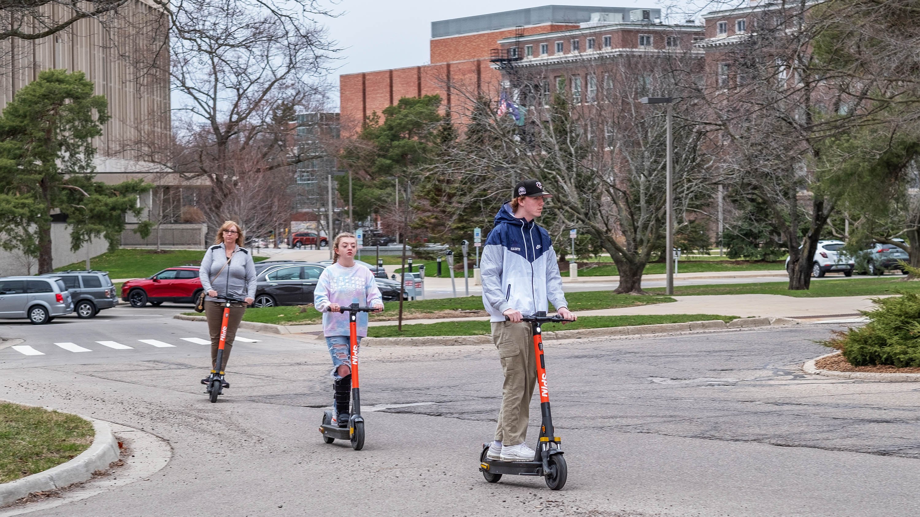 Three people riding electric scooters on campus