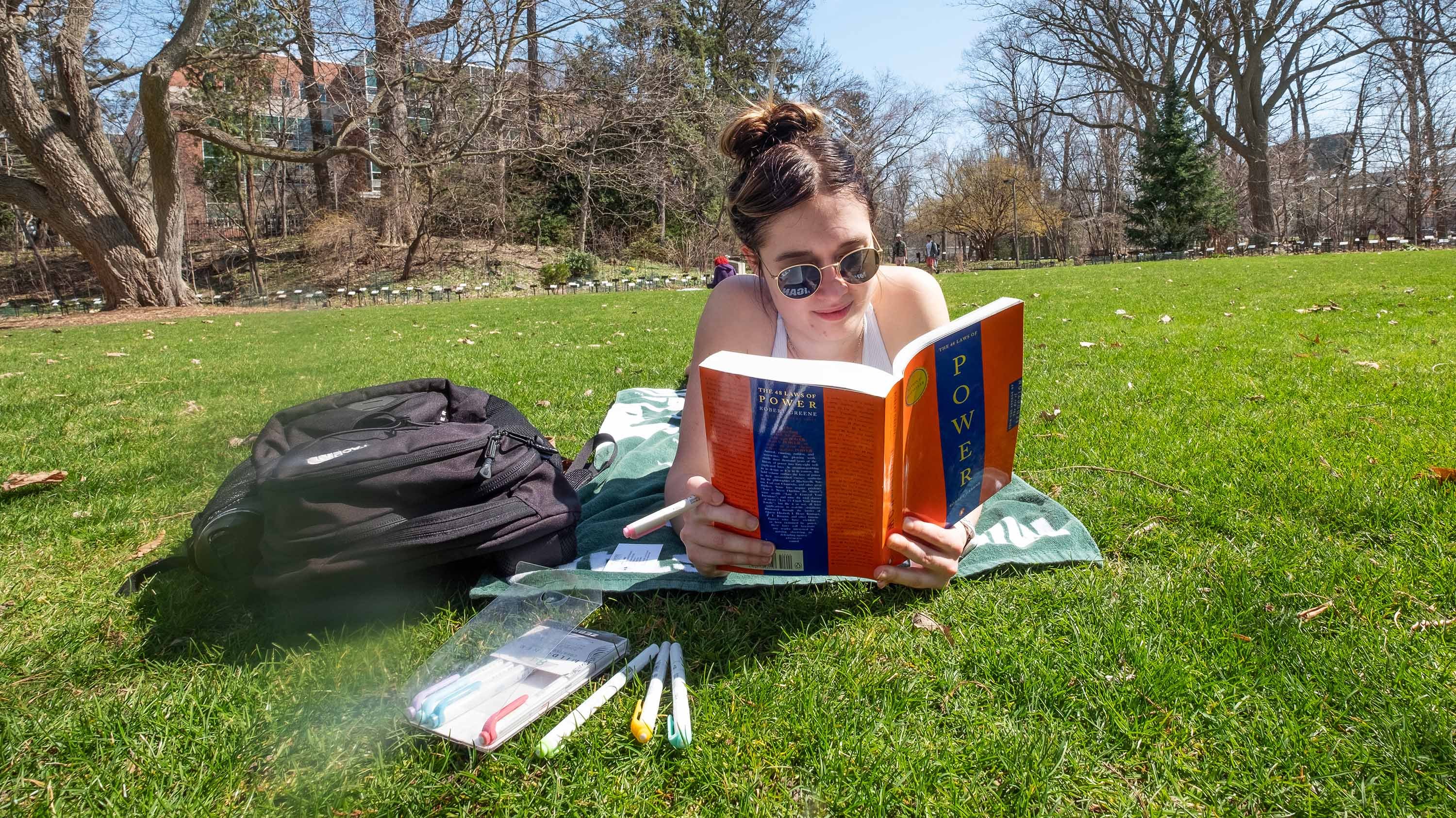 Student reading book lying in the grass, in Beal Botanical Garden