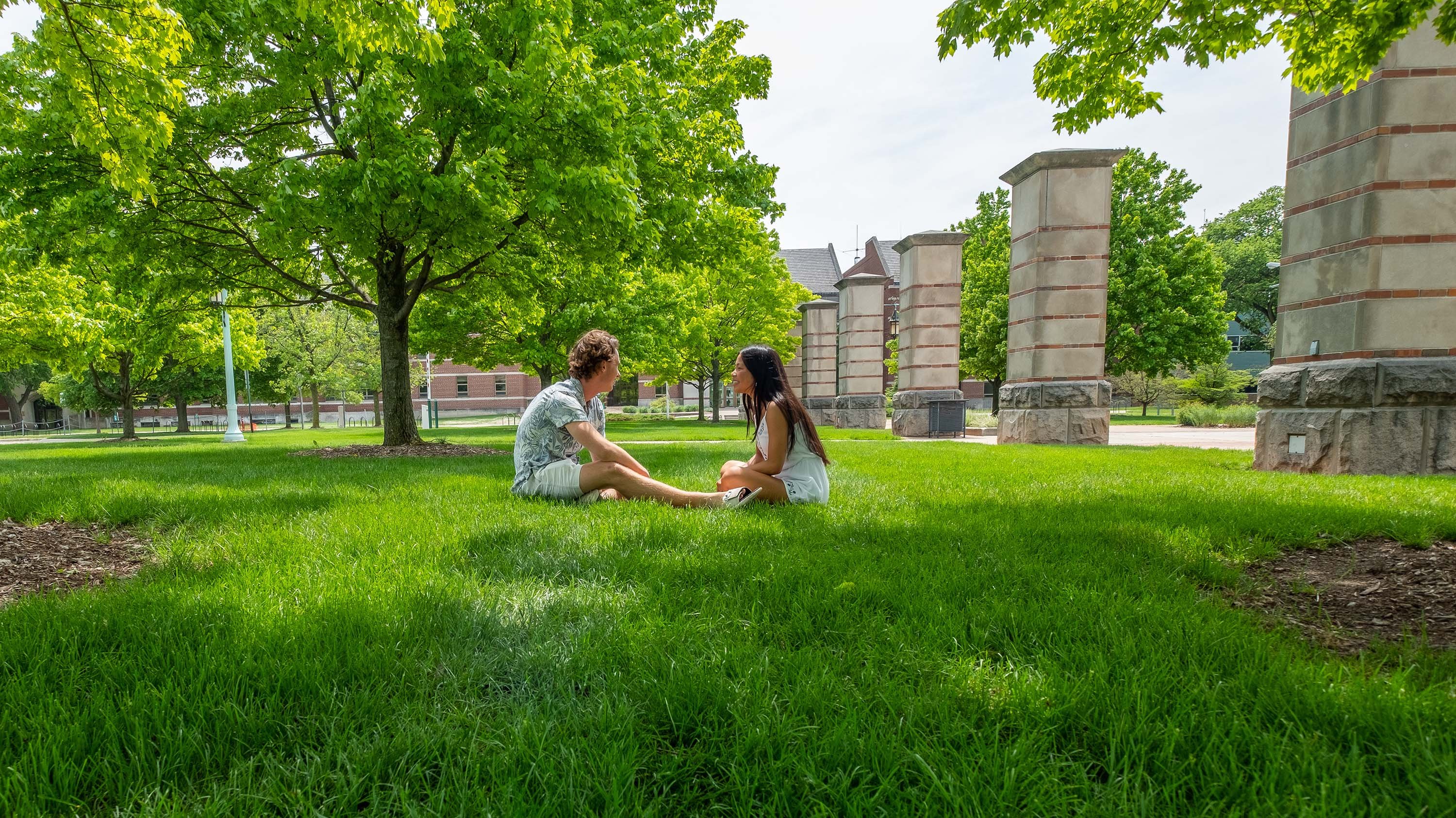 Two people sitting in the grass near Benefactor's Plaza