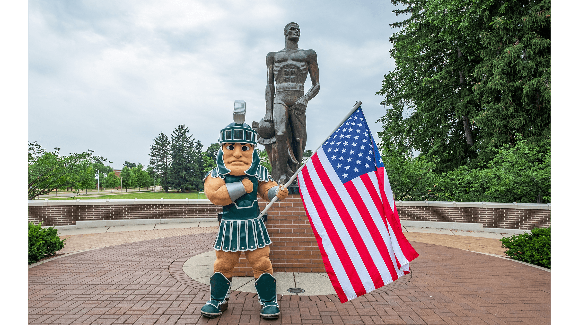 Sparty mascot waving American flag in front of the Spartan