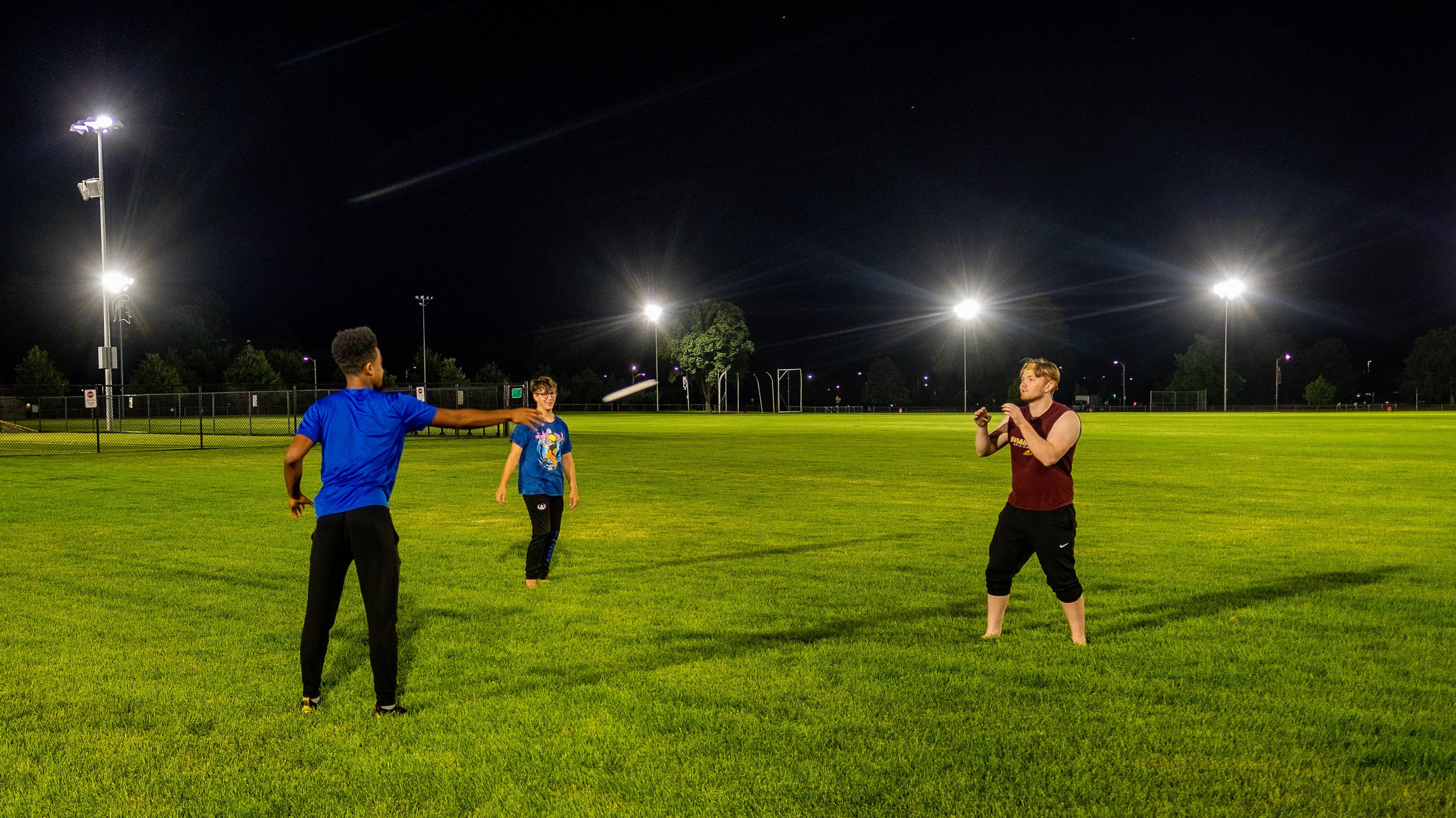 Three students playing frisbee in brightly lit field at night