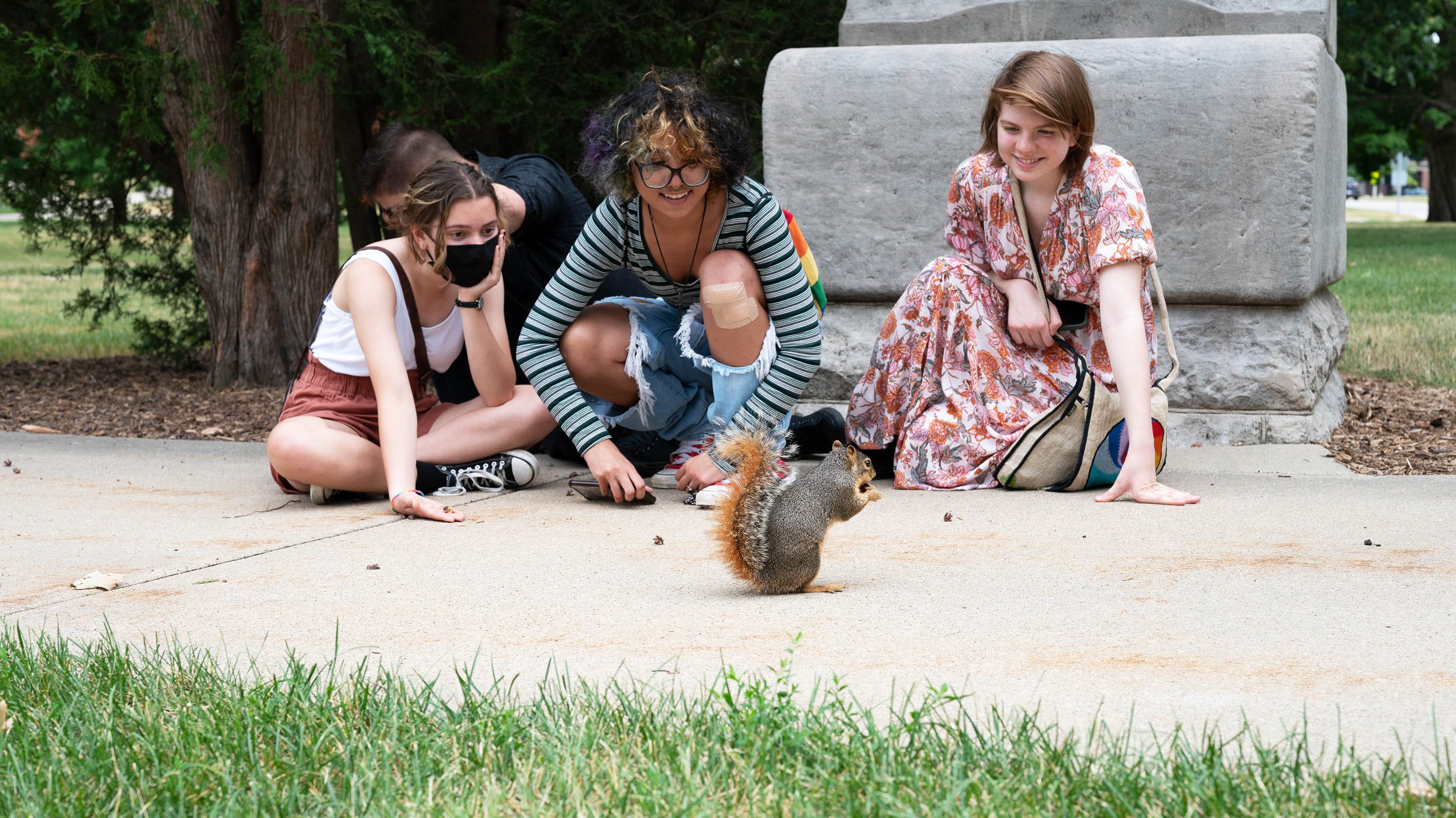 Three students sitting on the ground looking at a squirrel