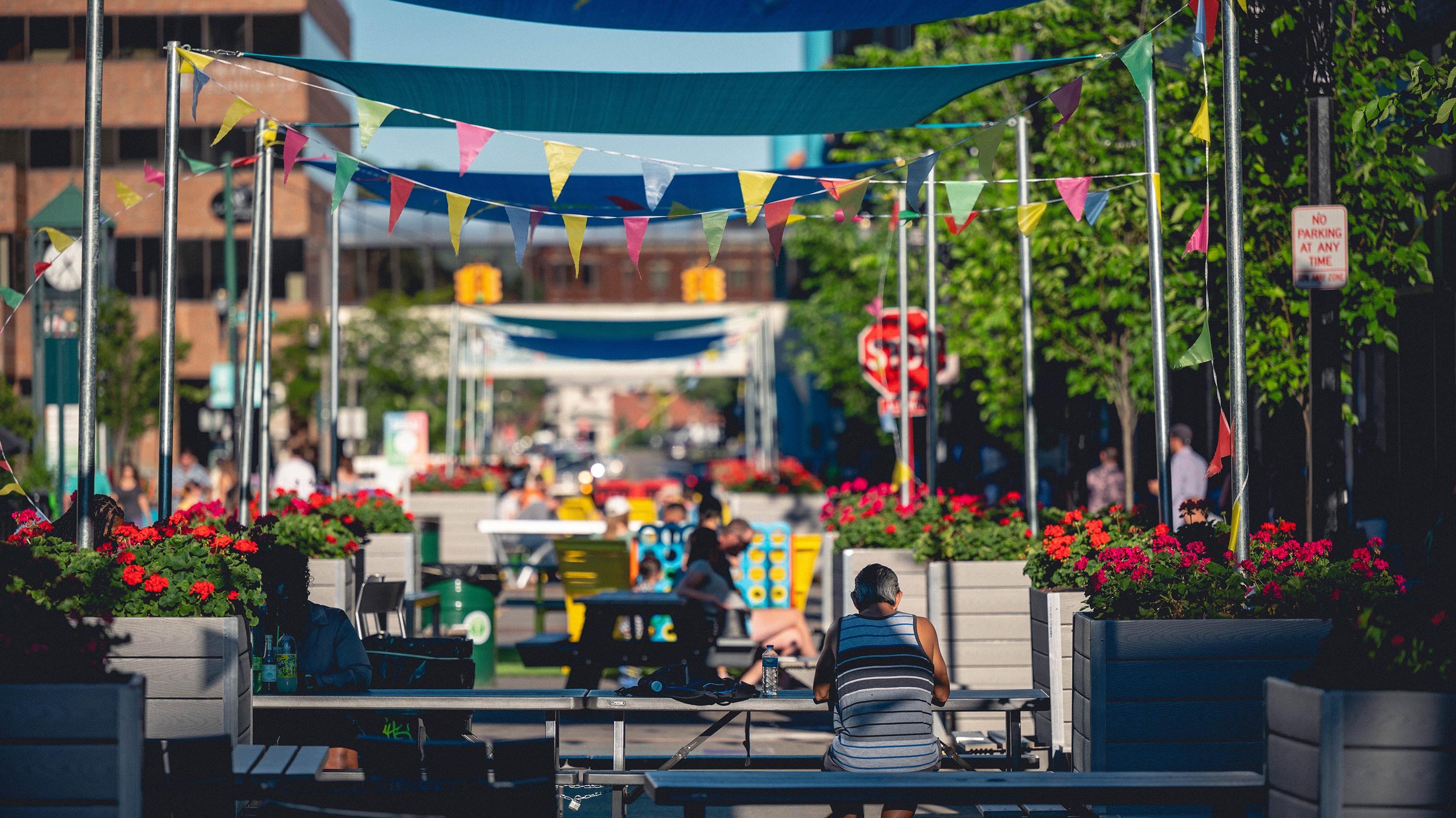People sitting at outdoor seating on Albert Ave under colorful penants