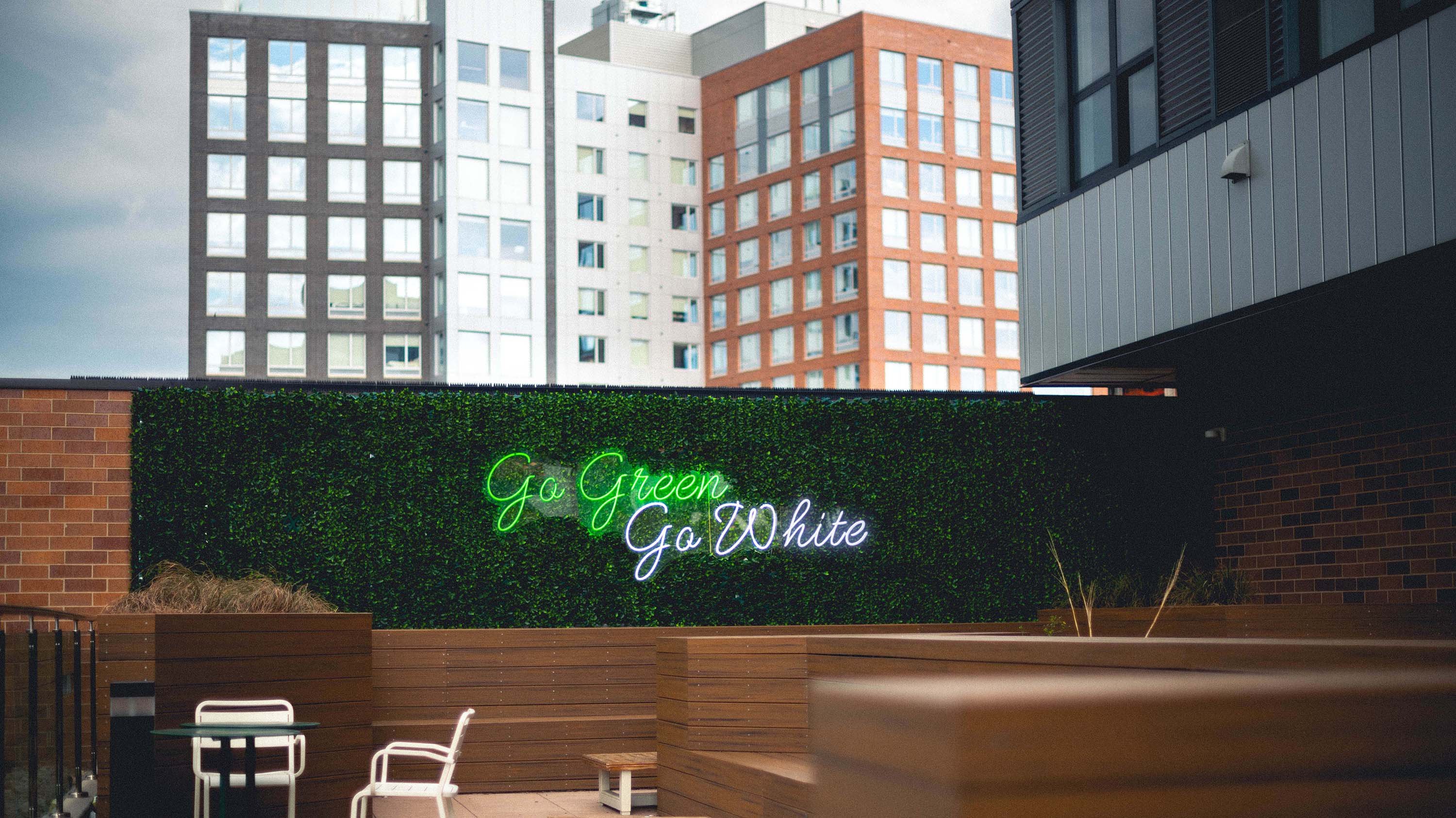 Neon sign that reads 'Go green, go white' on a foliage-covered wall on the amenity deck of The Landmark