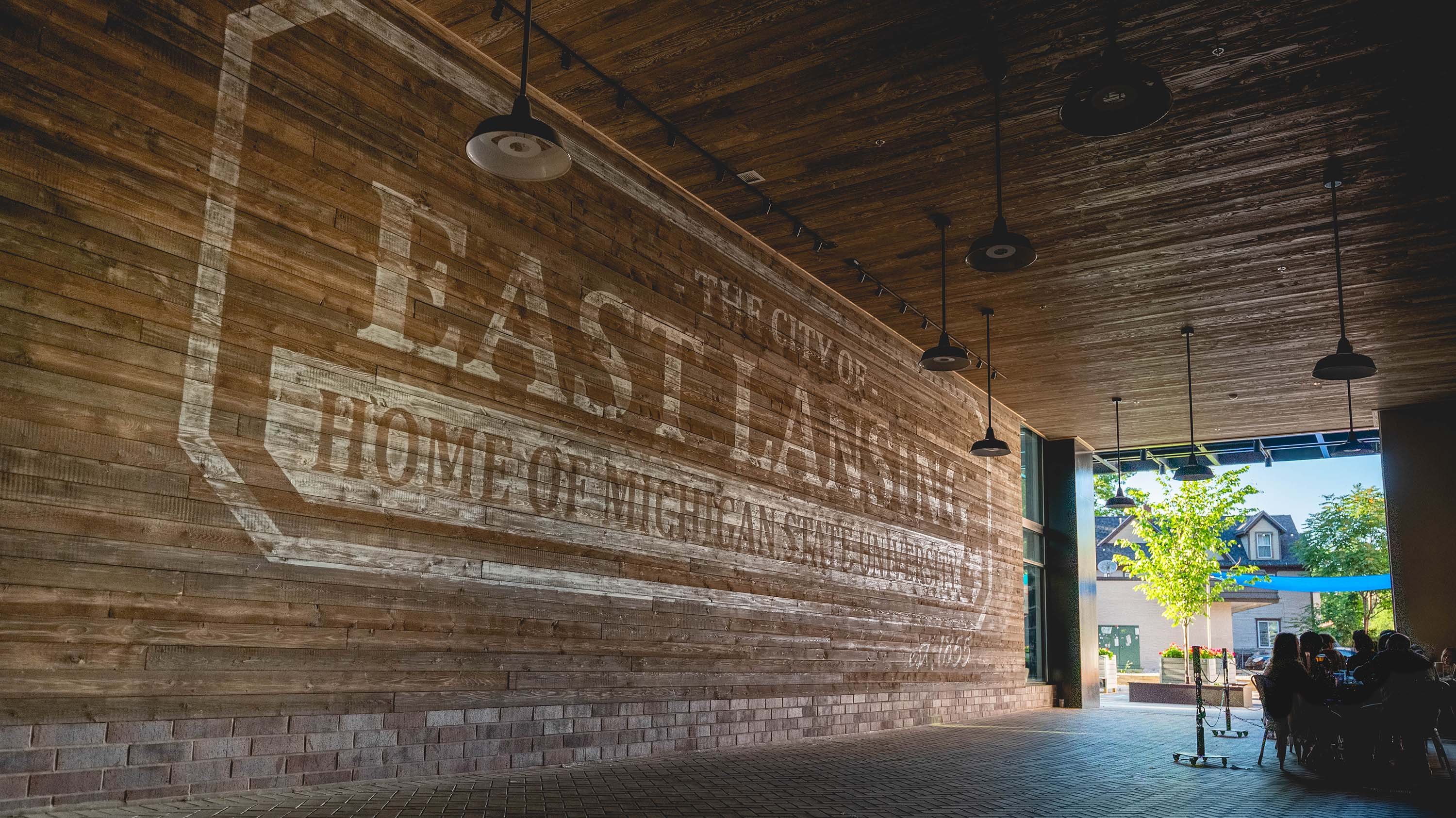 Large outdoor wooden sign that reads 'City of East Lansing, Home of Michigan State University'