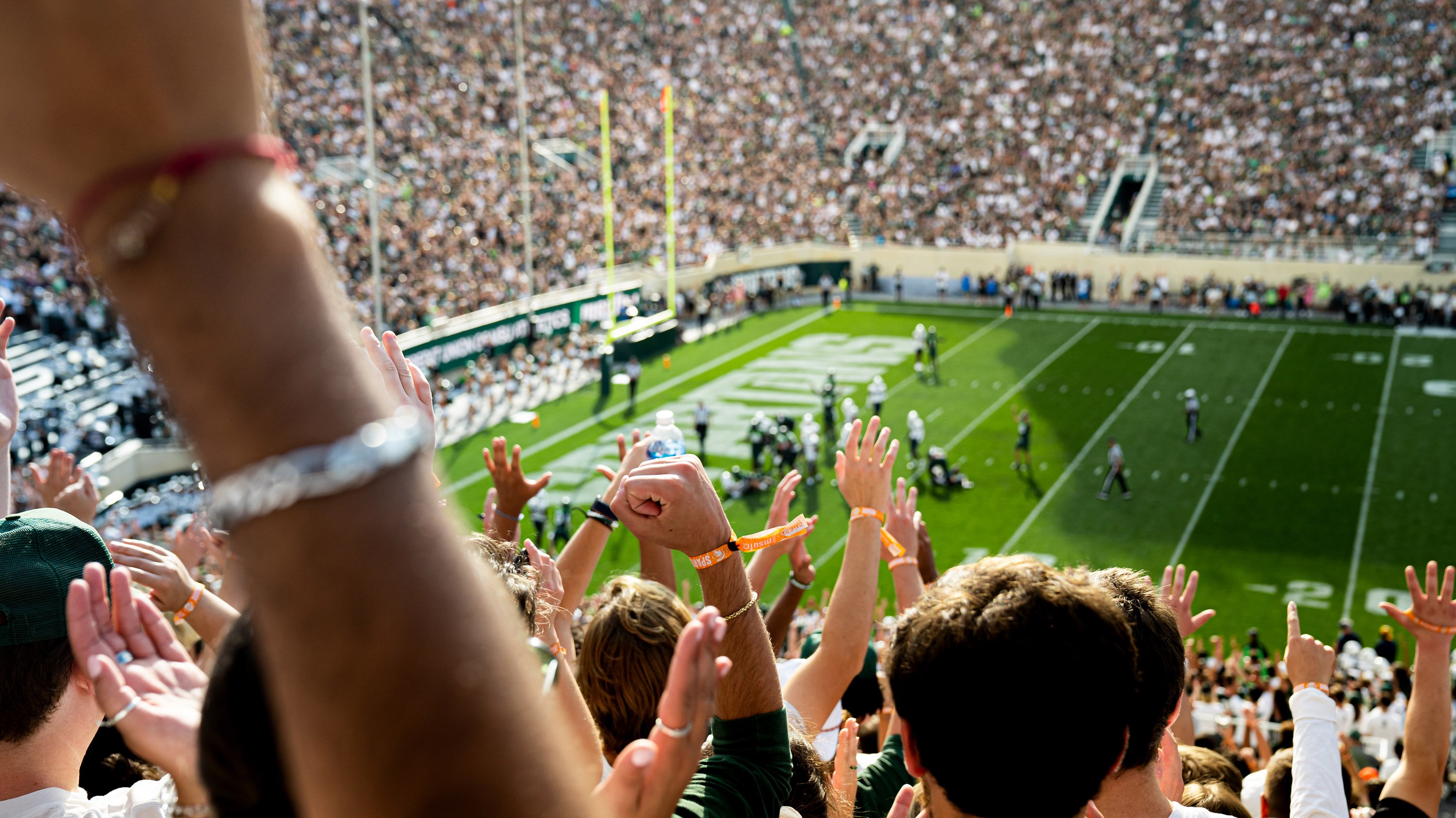 Spartan Stadium seen from the Student Section with hands of cheering fans in frame