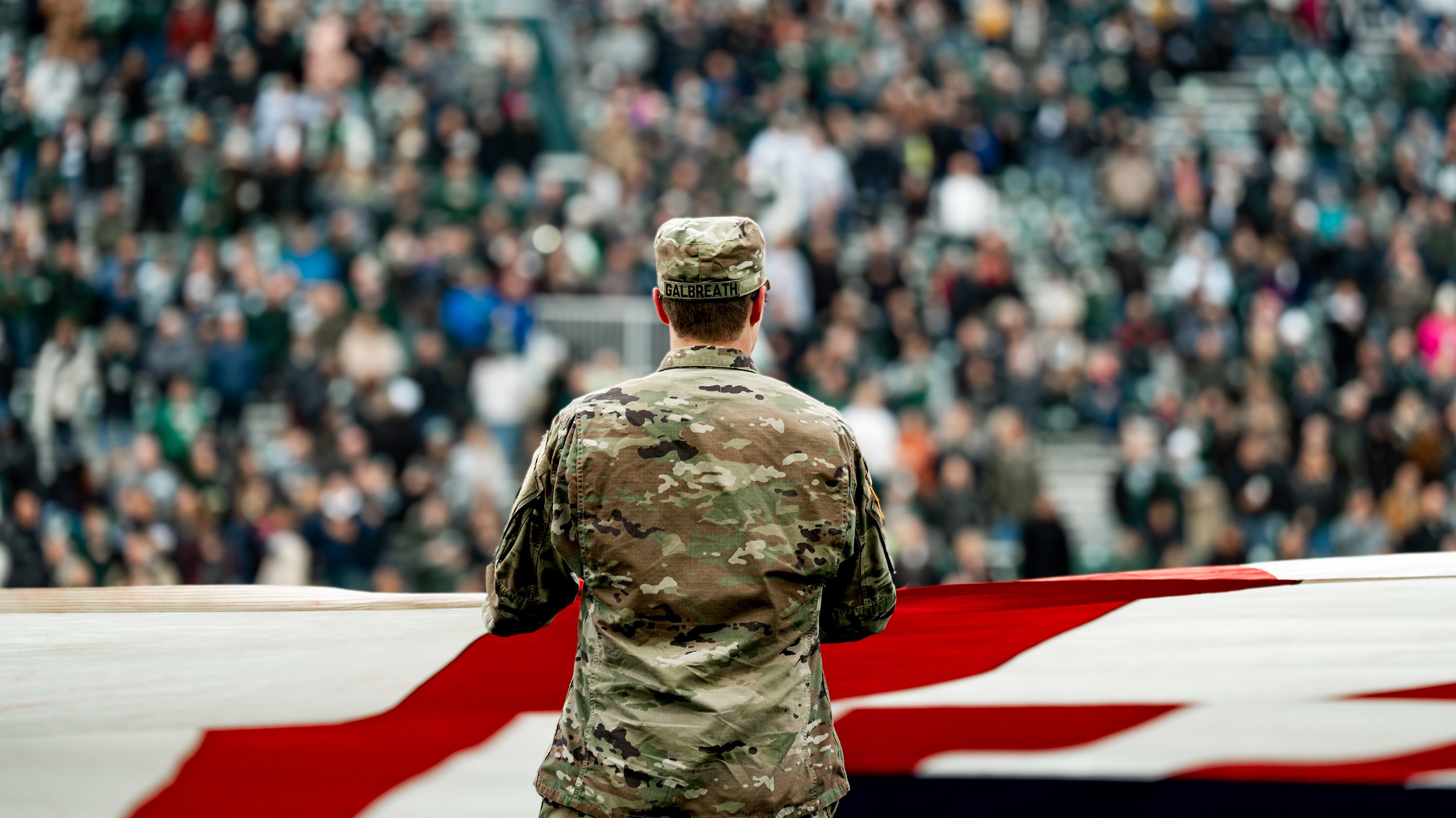 Member of ROTC holding giant American flag in Spartan Stadium