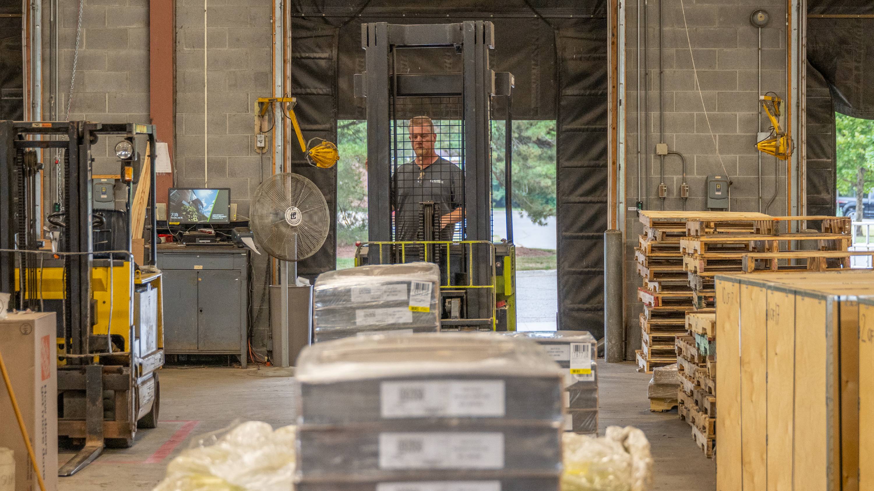 Boxes are stacked on pallets in the foreground. In the background, a man drives a forklift.