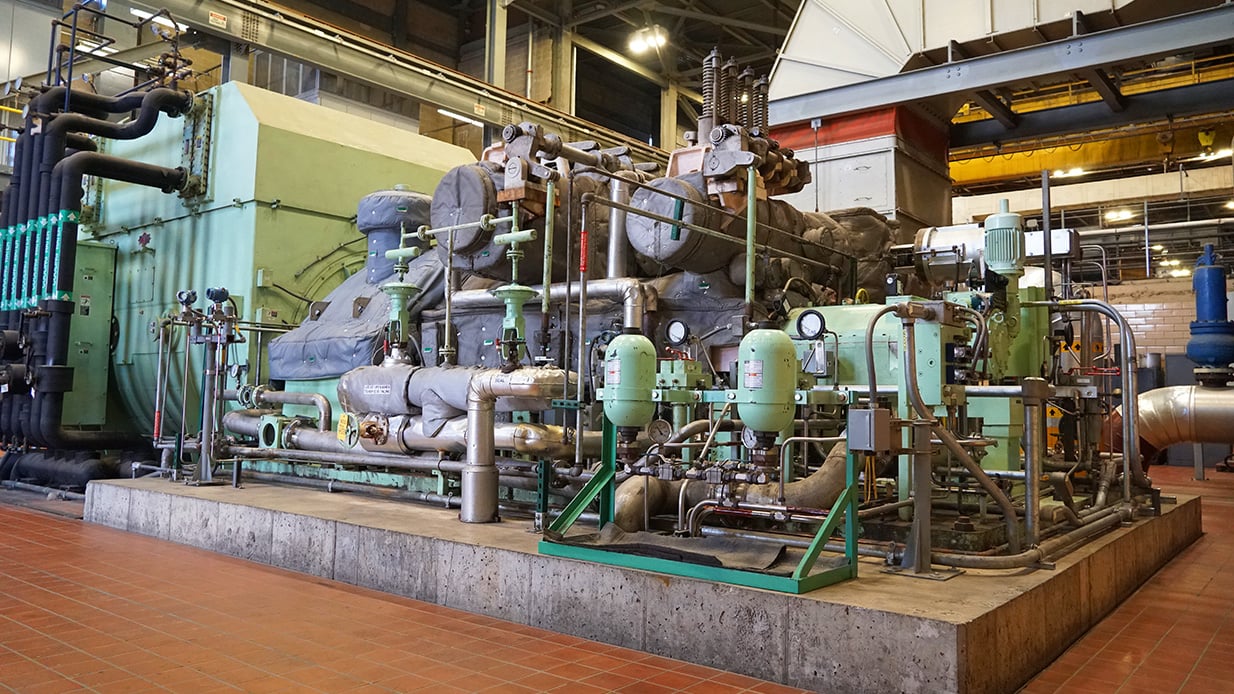 A large piece of equipment with multiple pipes and gauges sits on a cement pad.