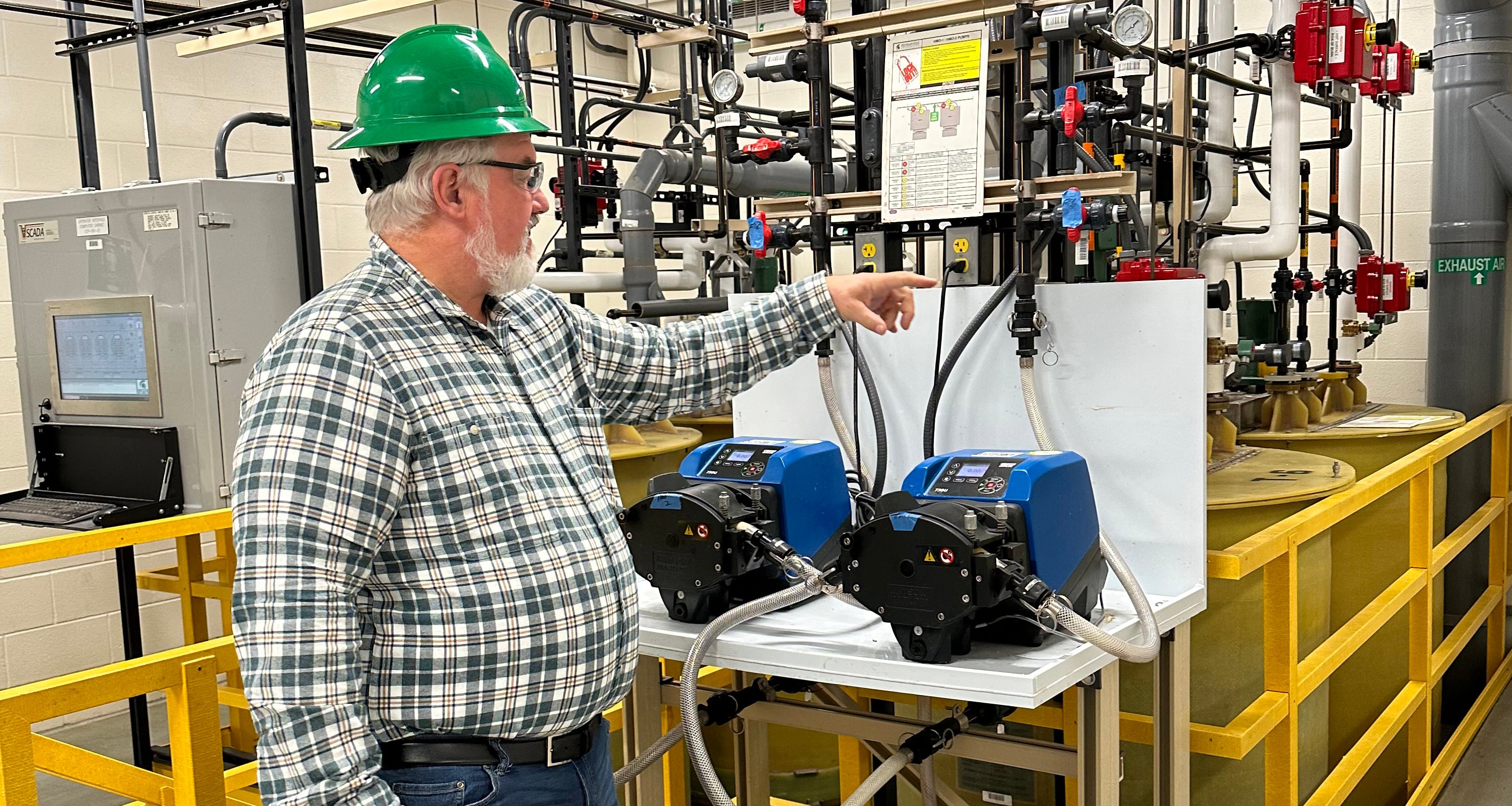 A worker in a green hard hat points at equipment.