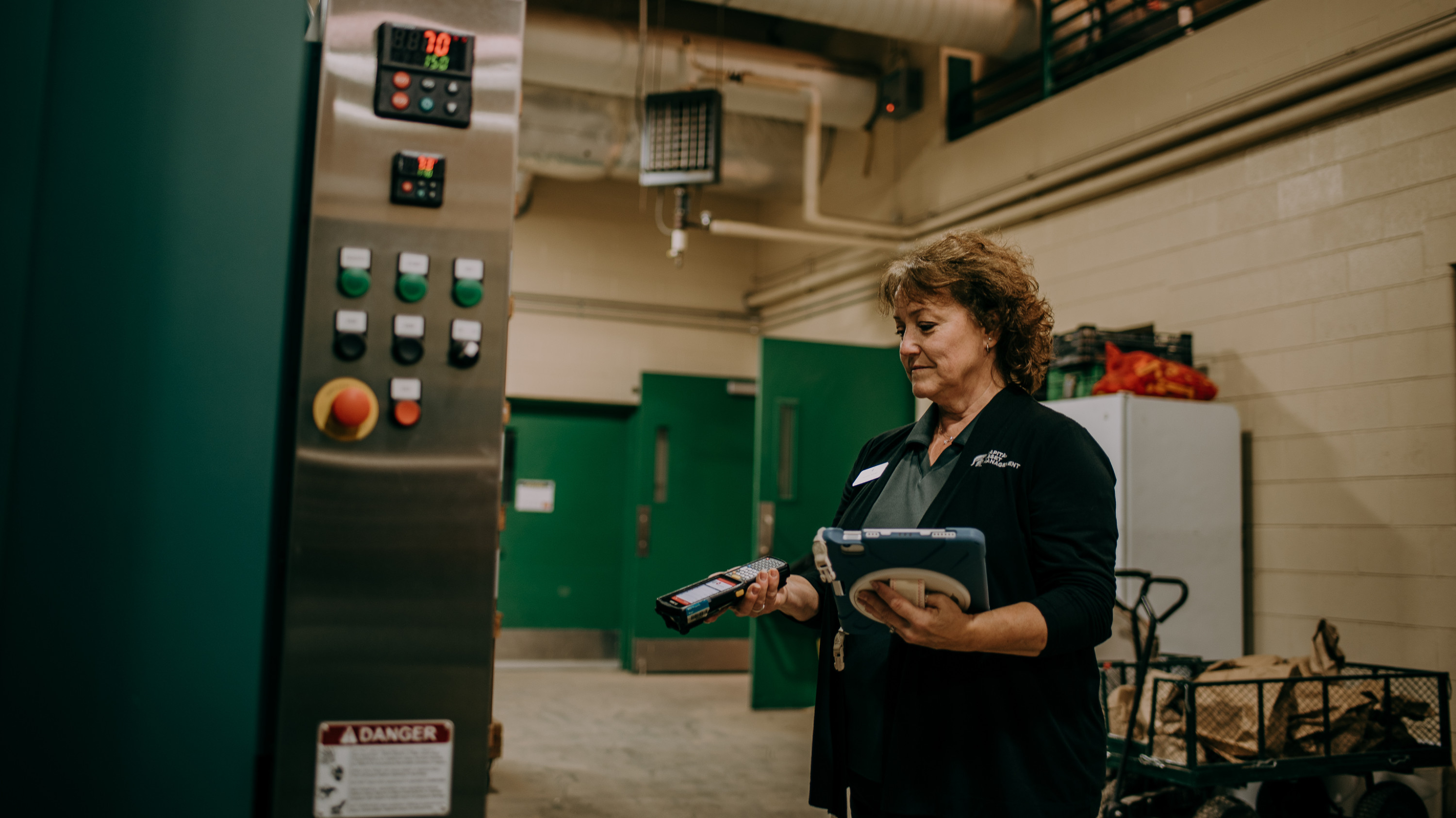 Debbie Smith, holding a hand scanner and tablet, looks at a piece of equipment during a routine audit.