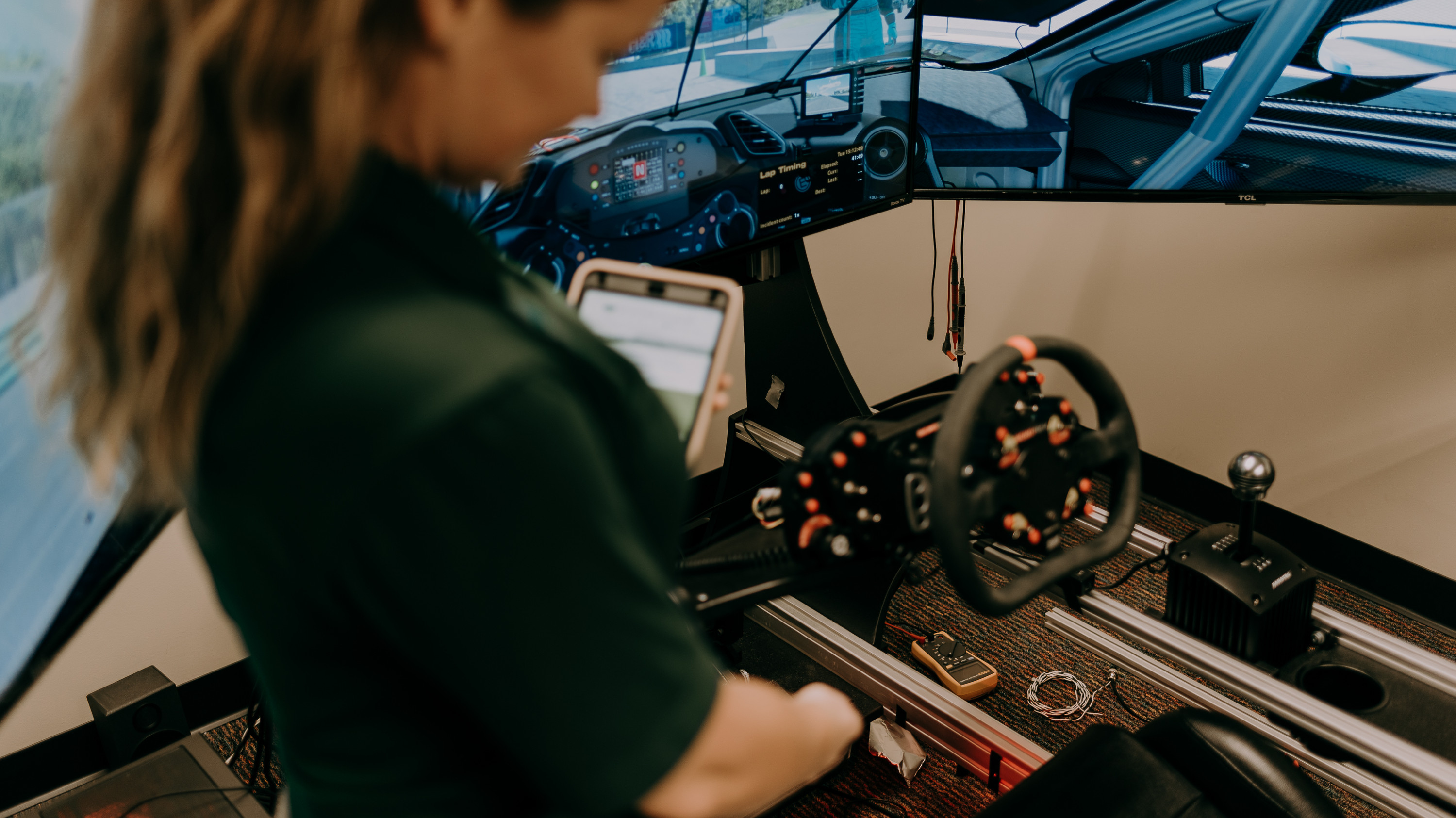 Anna Foster scans the asset tag on a black and red car simulator with seat, steering wheel and colorful dials in background.