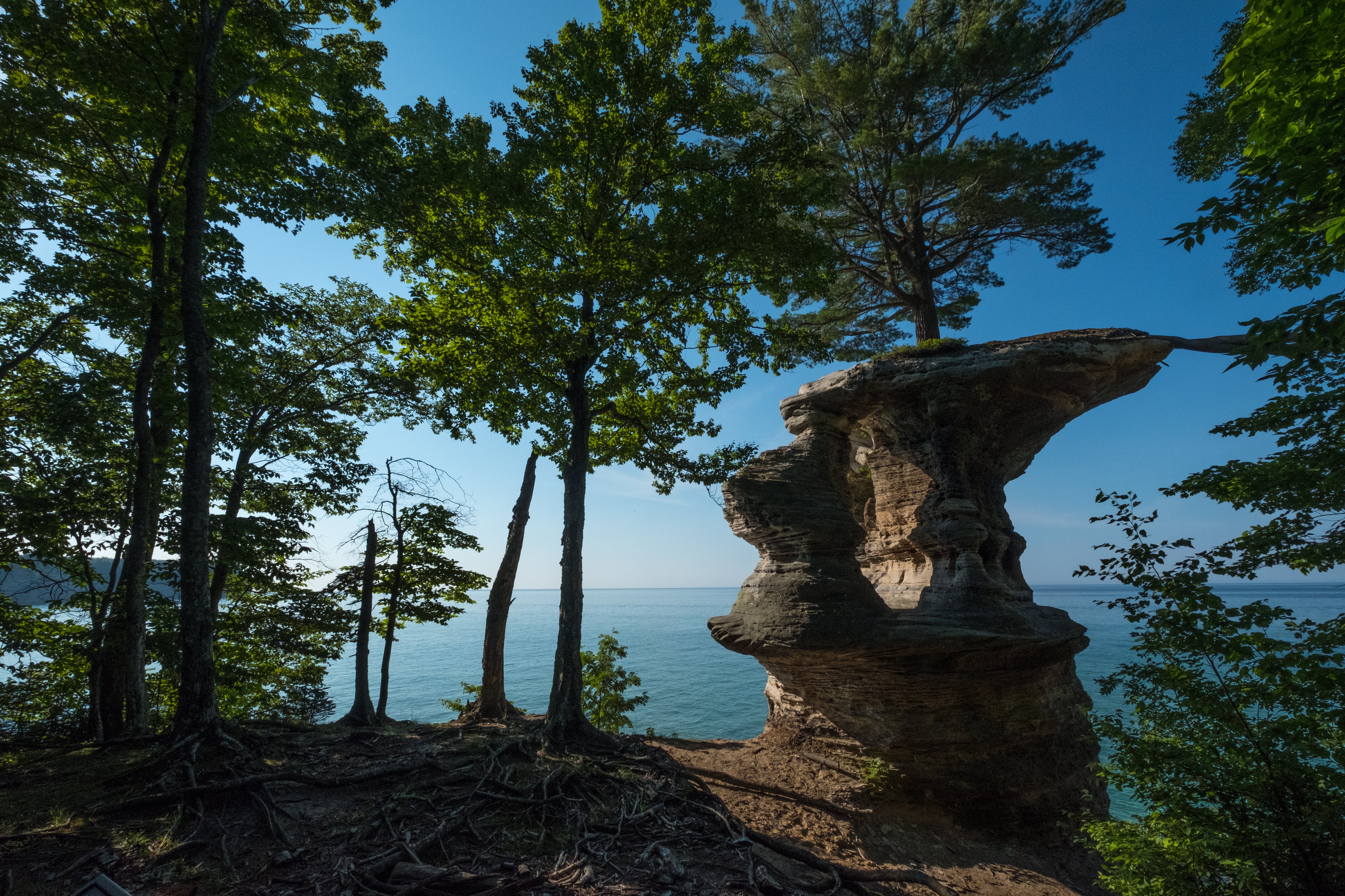 Rock formation juts into the sky next to leaf-covered trees with a view of Lake Superior in Michigan's Upper Penninusla