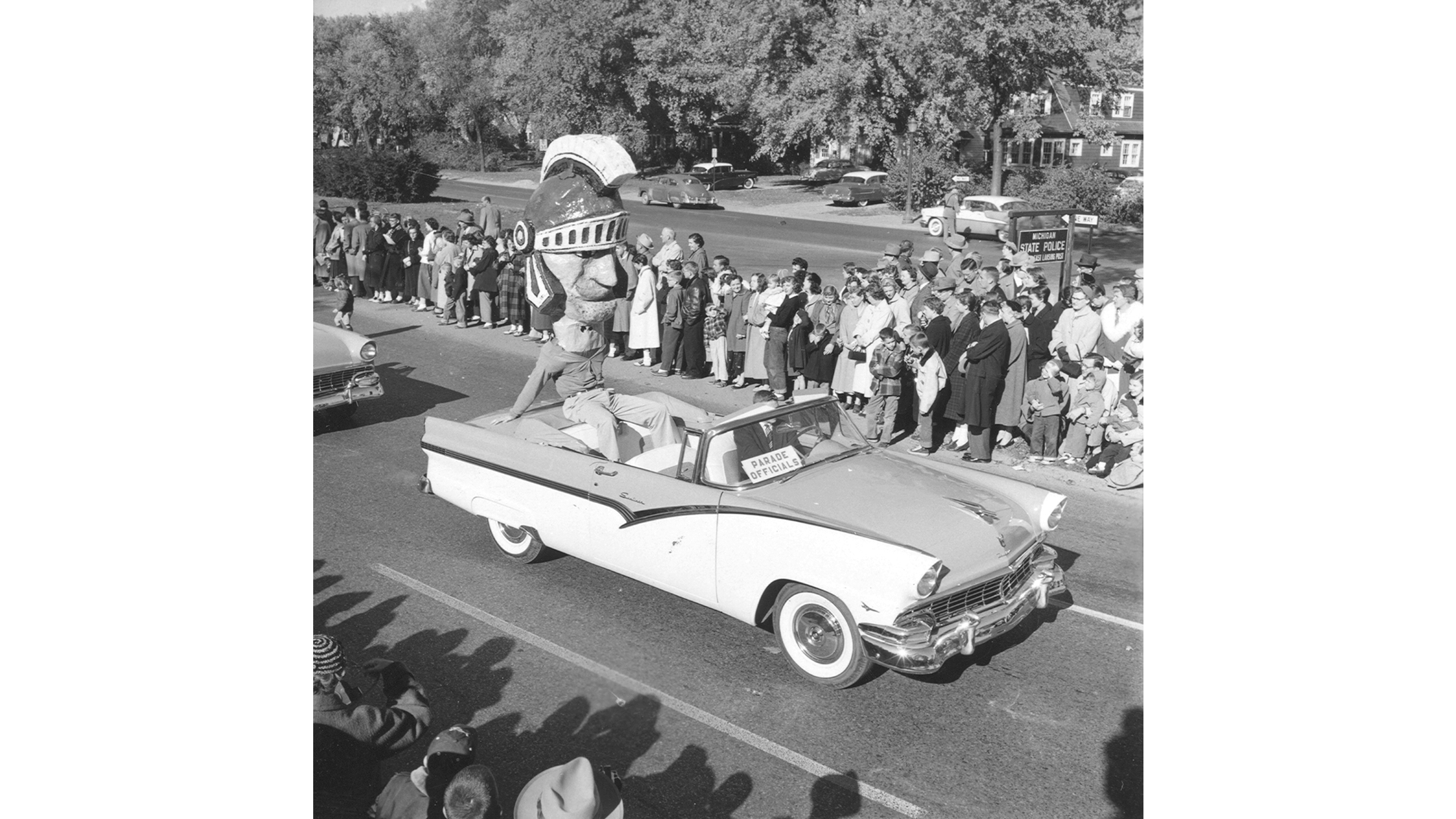 Vintage photo of 1955 homecoming parade, with Sparty mascot riding in a car