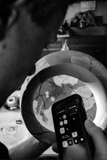 a smartphone is used to illuminate the interior of a Roman-era cooking pot in search of the object’s catalogue number.