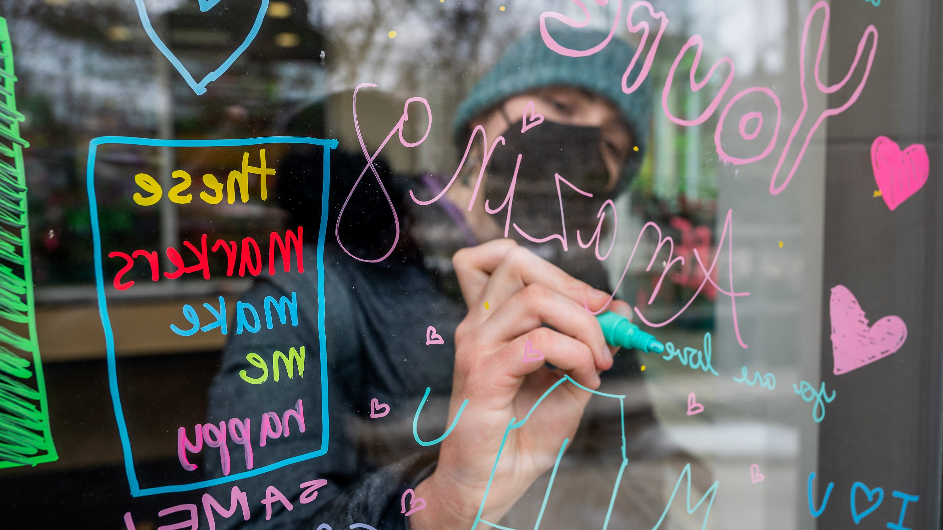 Person writing a message on library window, full of other messages of positivity for MSU