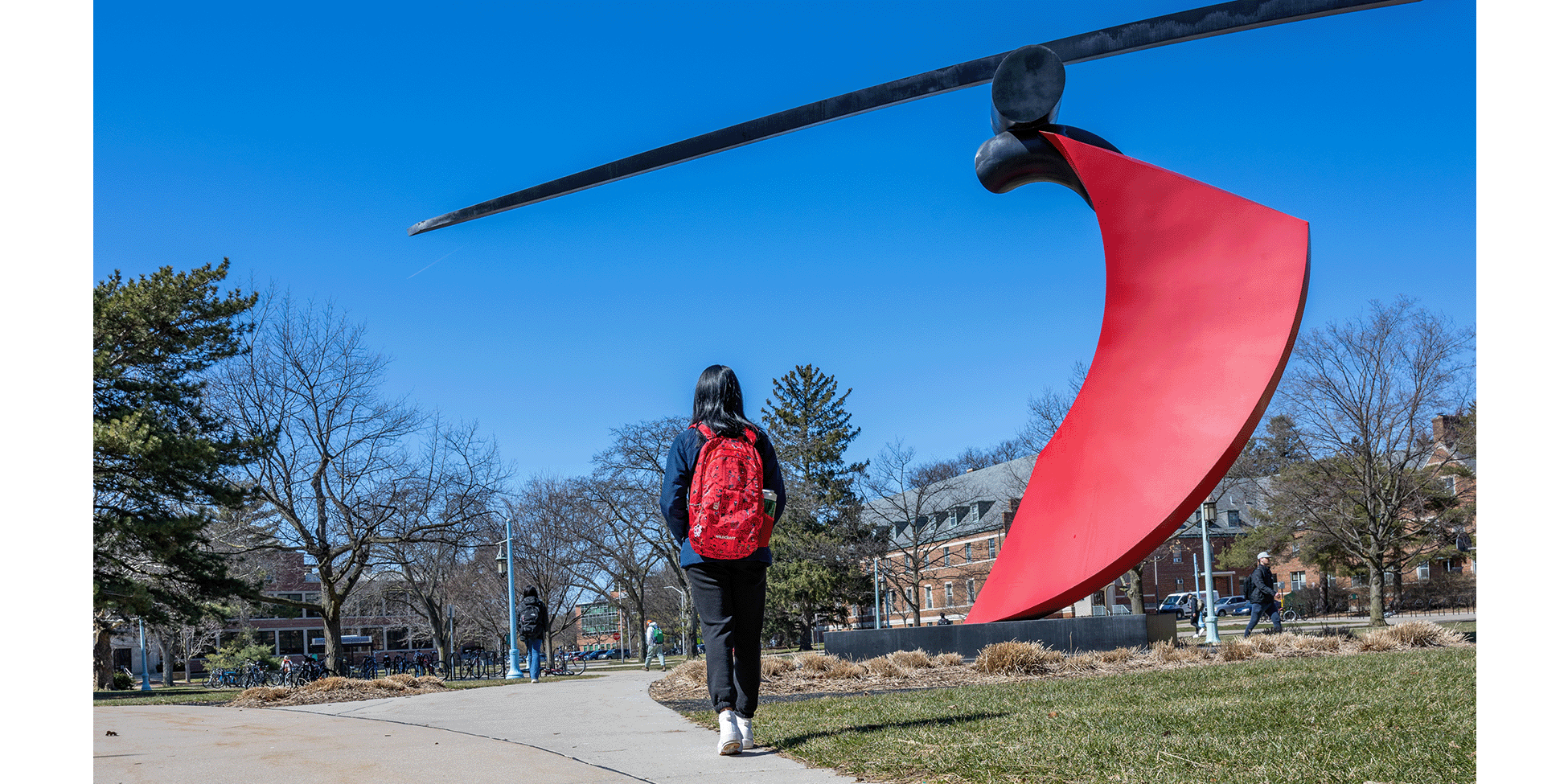 Student with red backpack walking near Funambulist sculpture