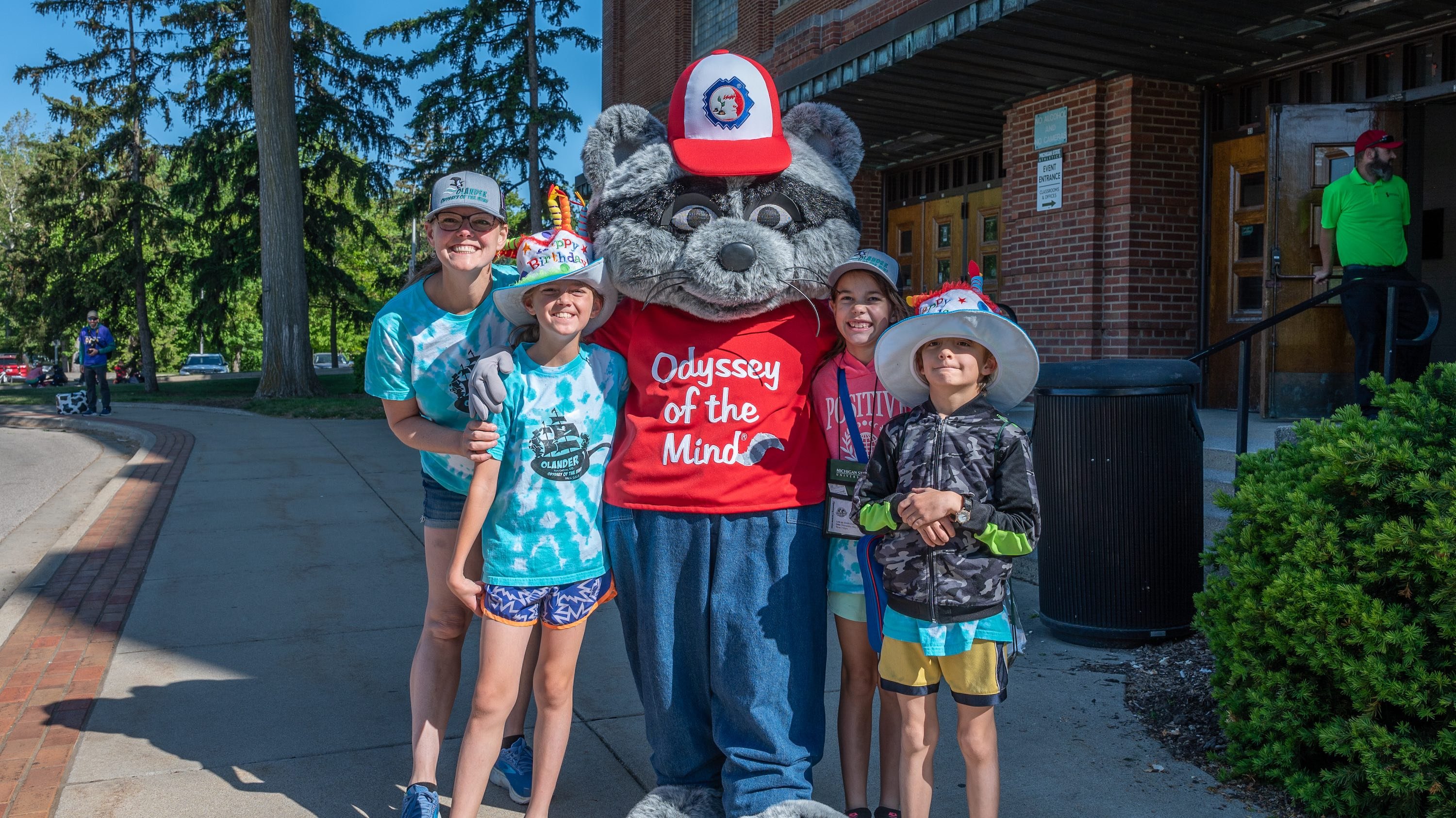 Participants at the Odyssey of the Mind World Finals pose with the event mascot outside Jenison