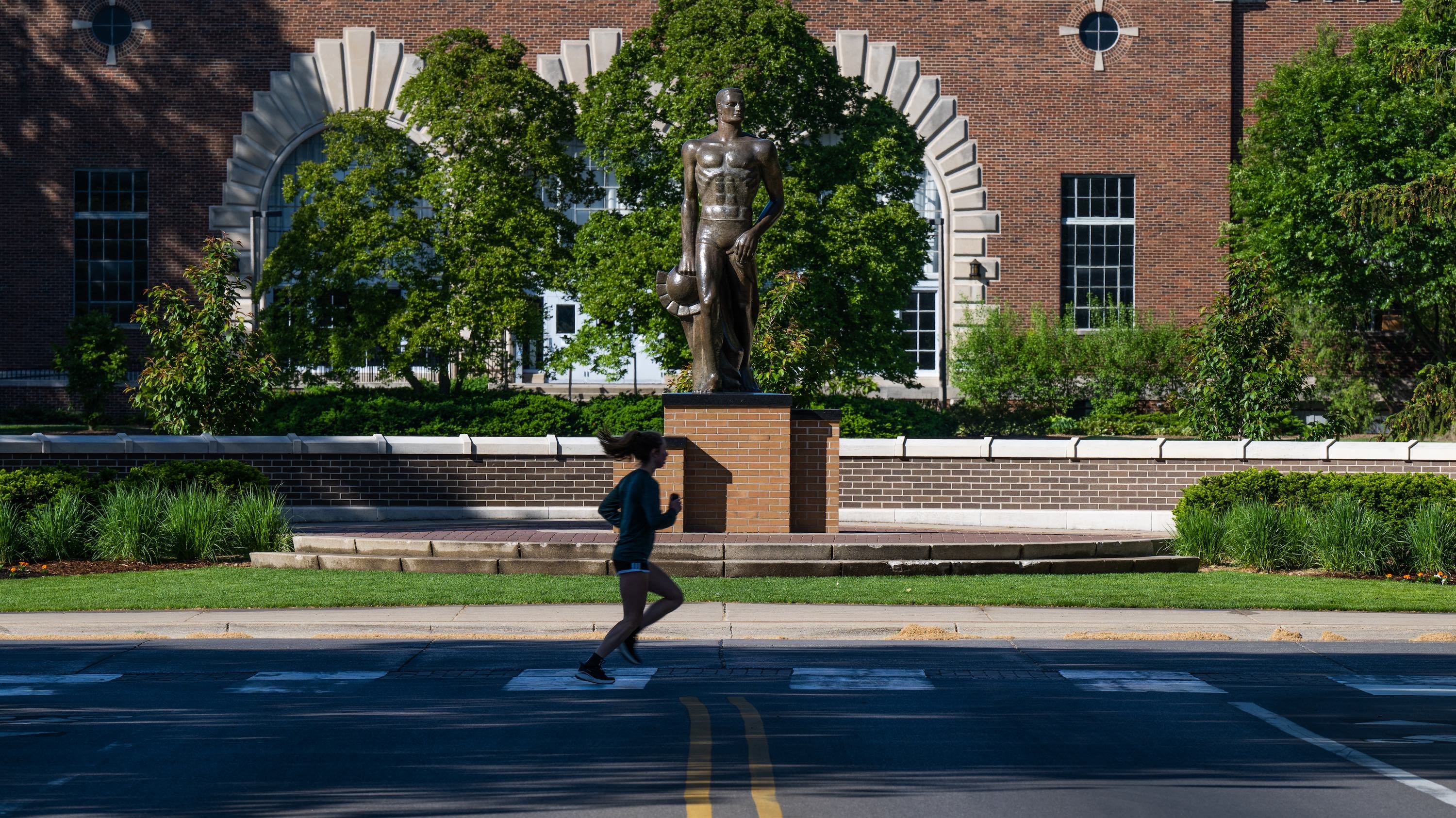 A runner crosses the street in front of The Spartan Statue