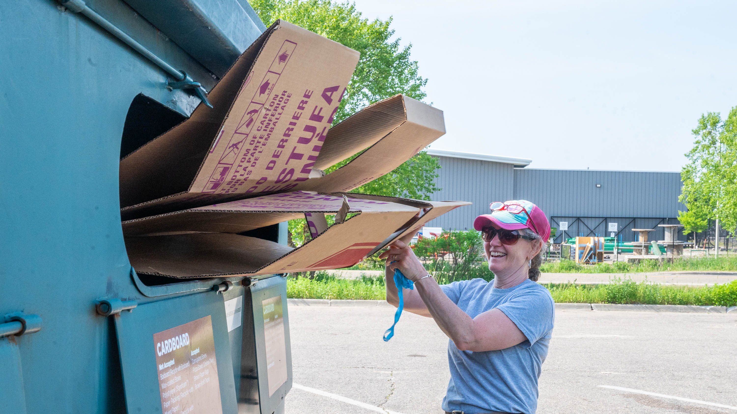 A person putting cardboard boxes into a recycling bin