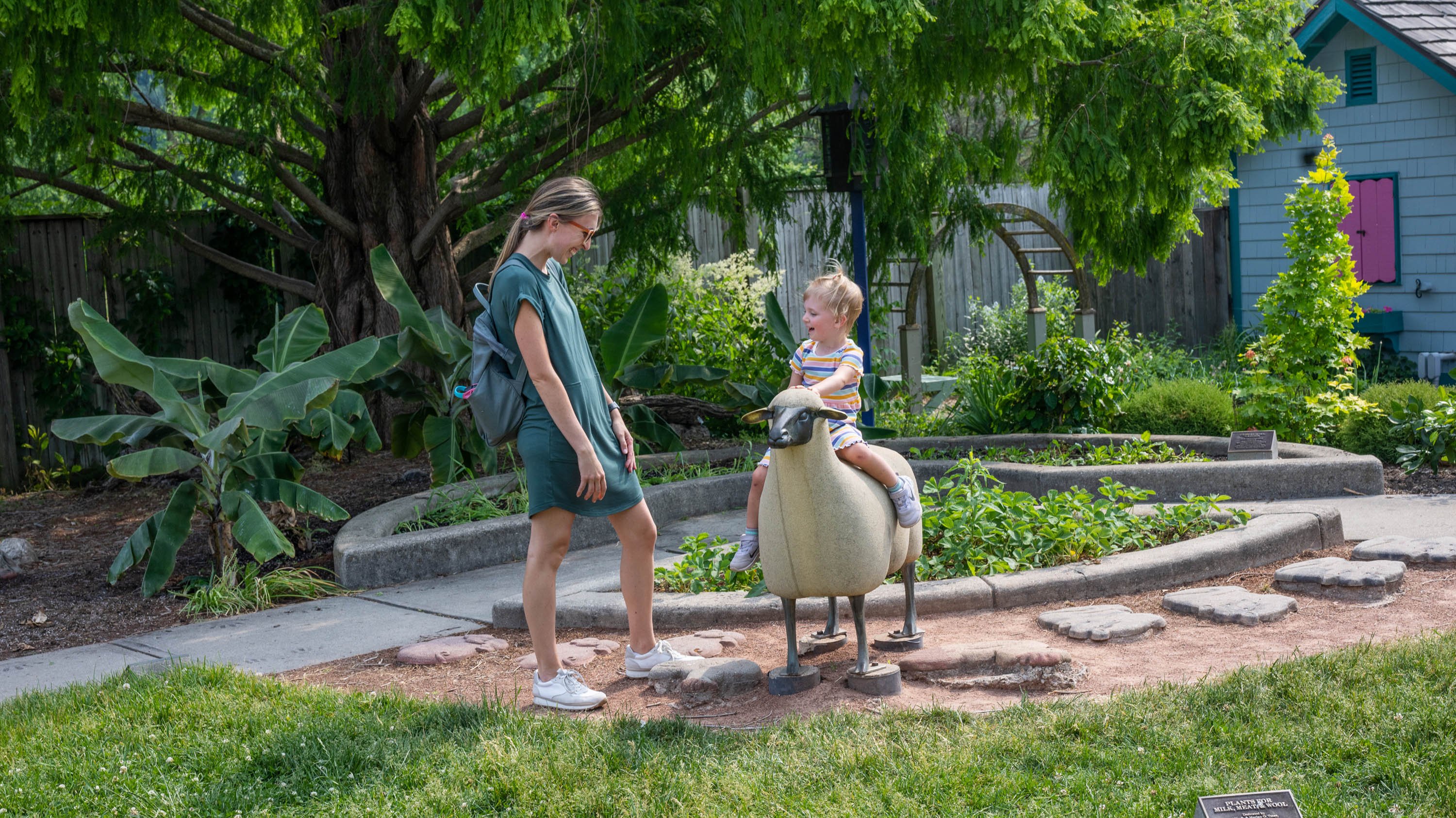 A child on top of a sheep sculpture in the Children's Garden, next to an adult visitor