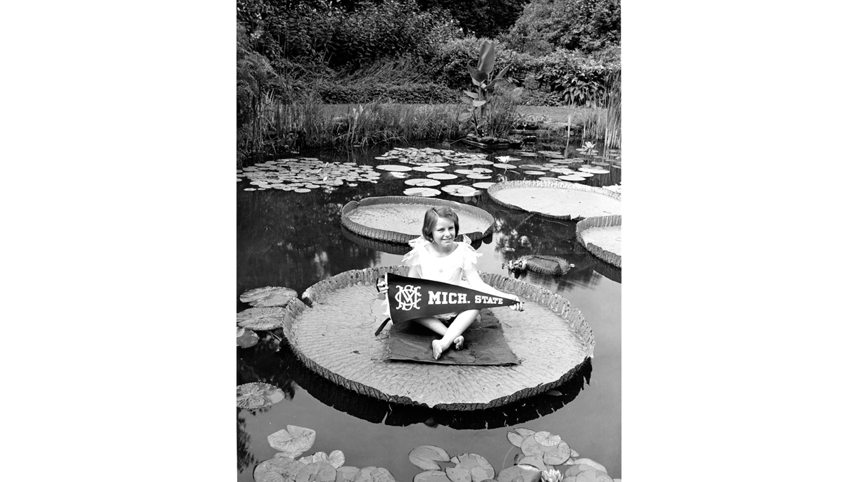 Small child sitting on lily pad with Michigan State pennant
