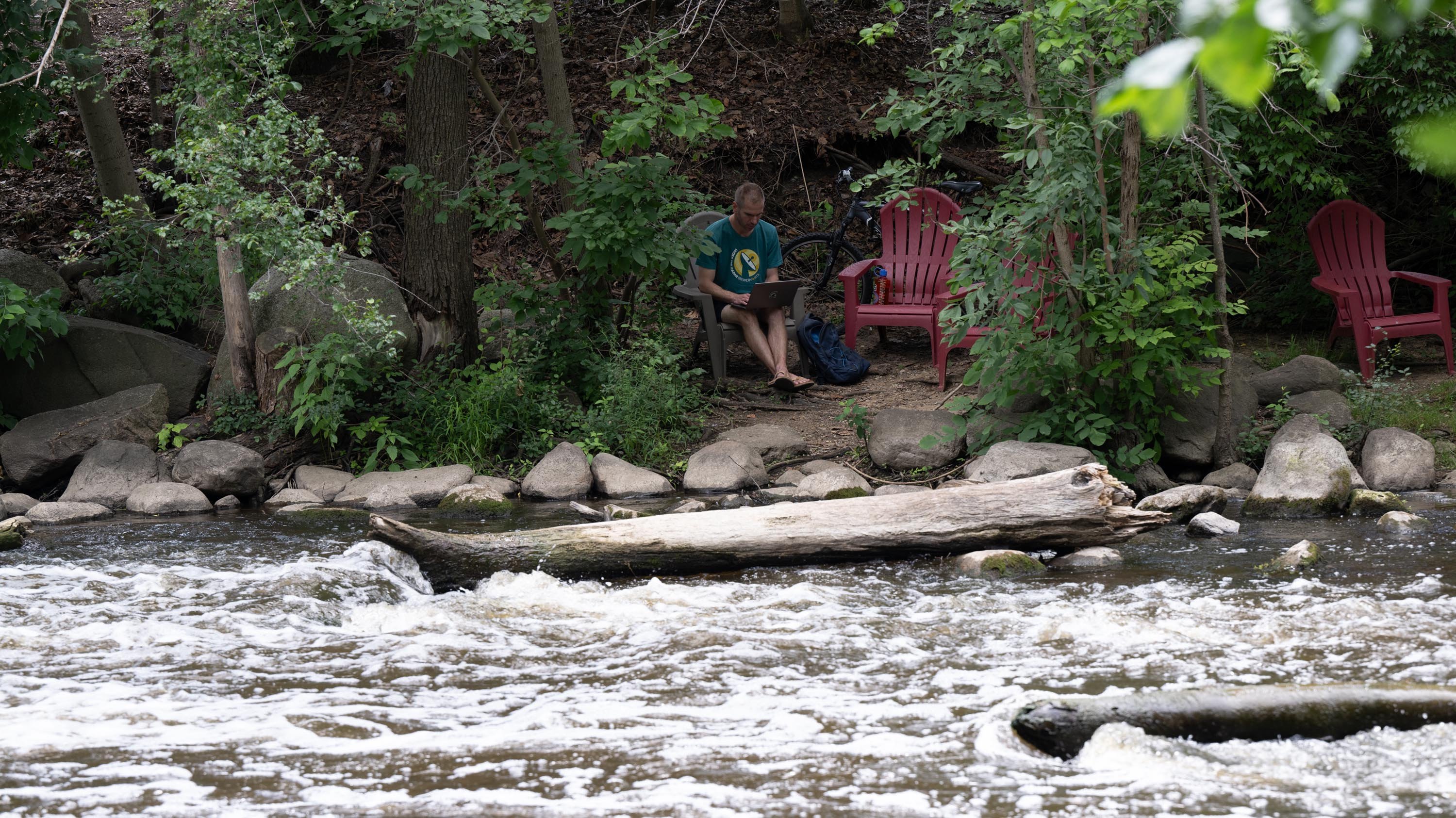 Person sitting in chair by the Red Cedar River