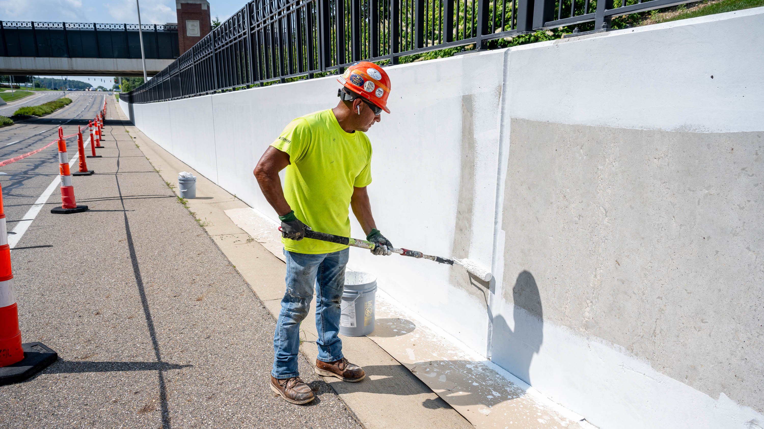 Construction worker painting bridge wall white