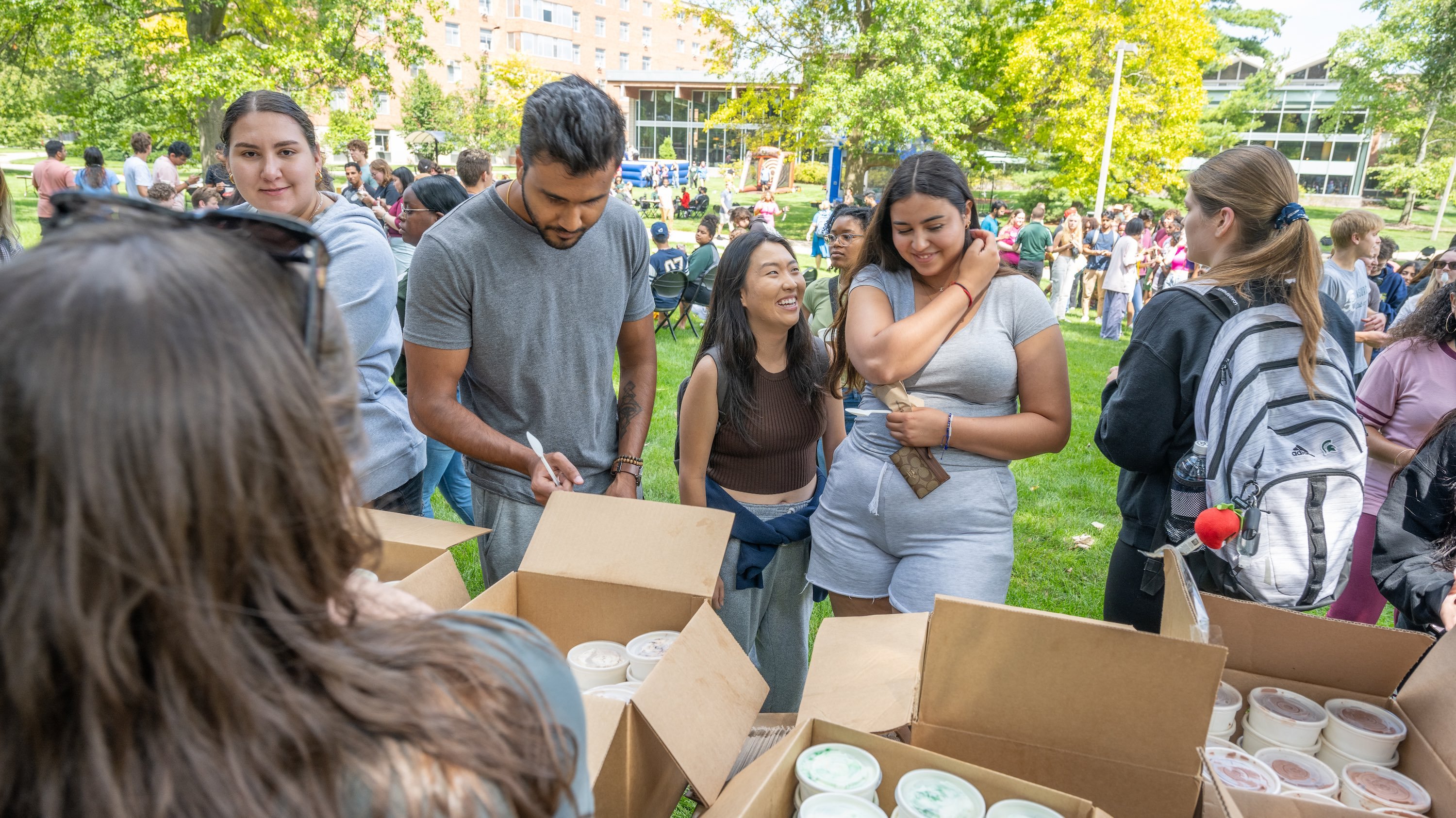 Smiling members of the MSU community gather around boxes filled with ice cream snacks