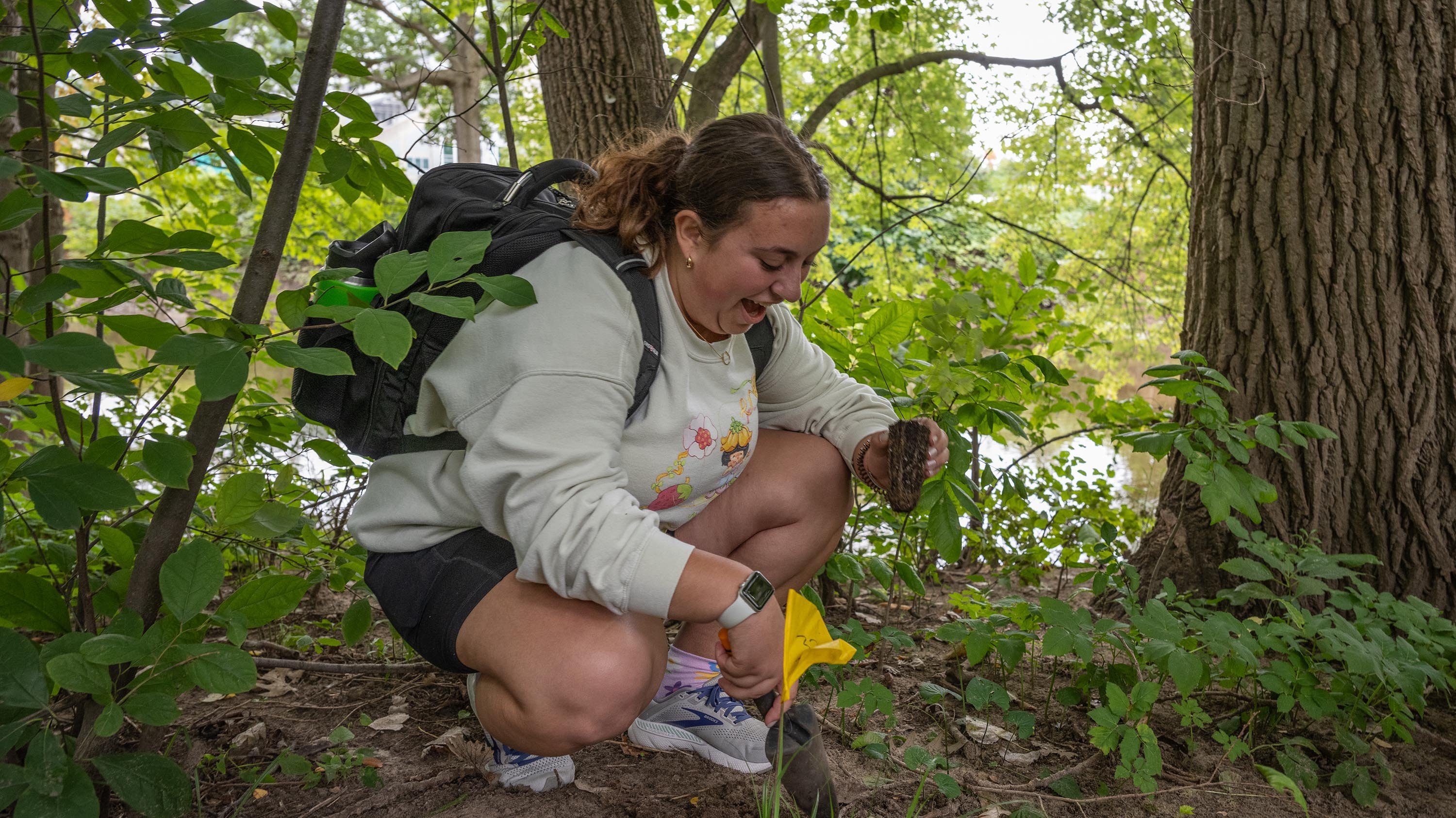 Student planting a native seedling by the Red Cedar river