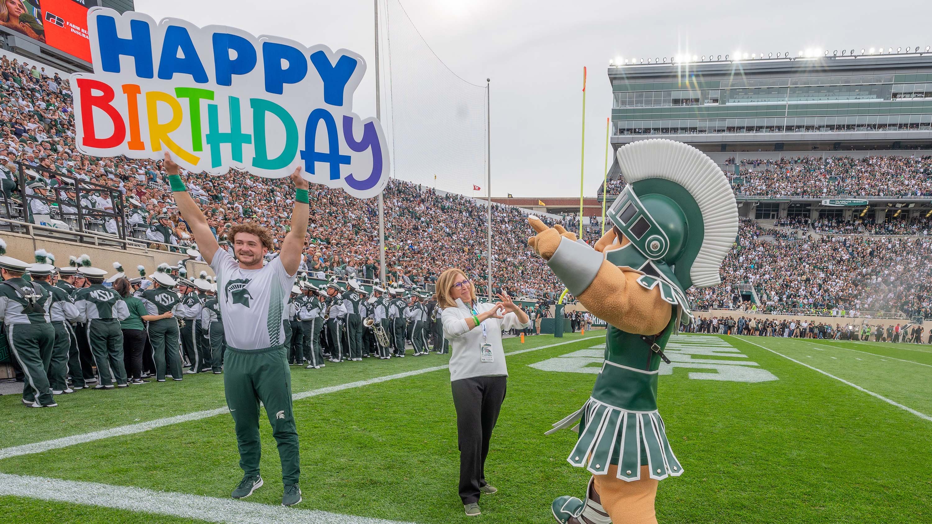 Spartan cheerleader holding 'happy birthday sign', Sparty and Theresa K. Woodruff 