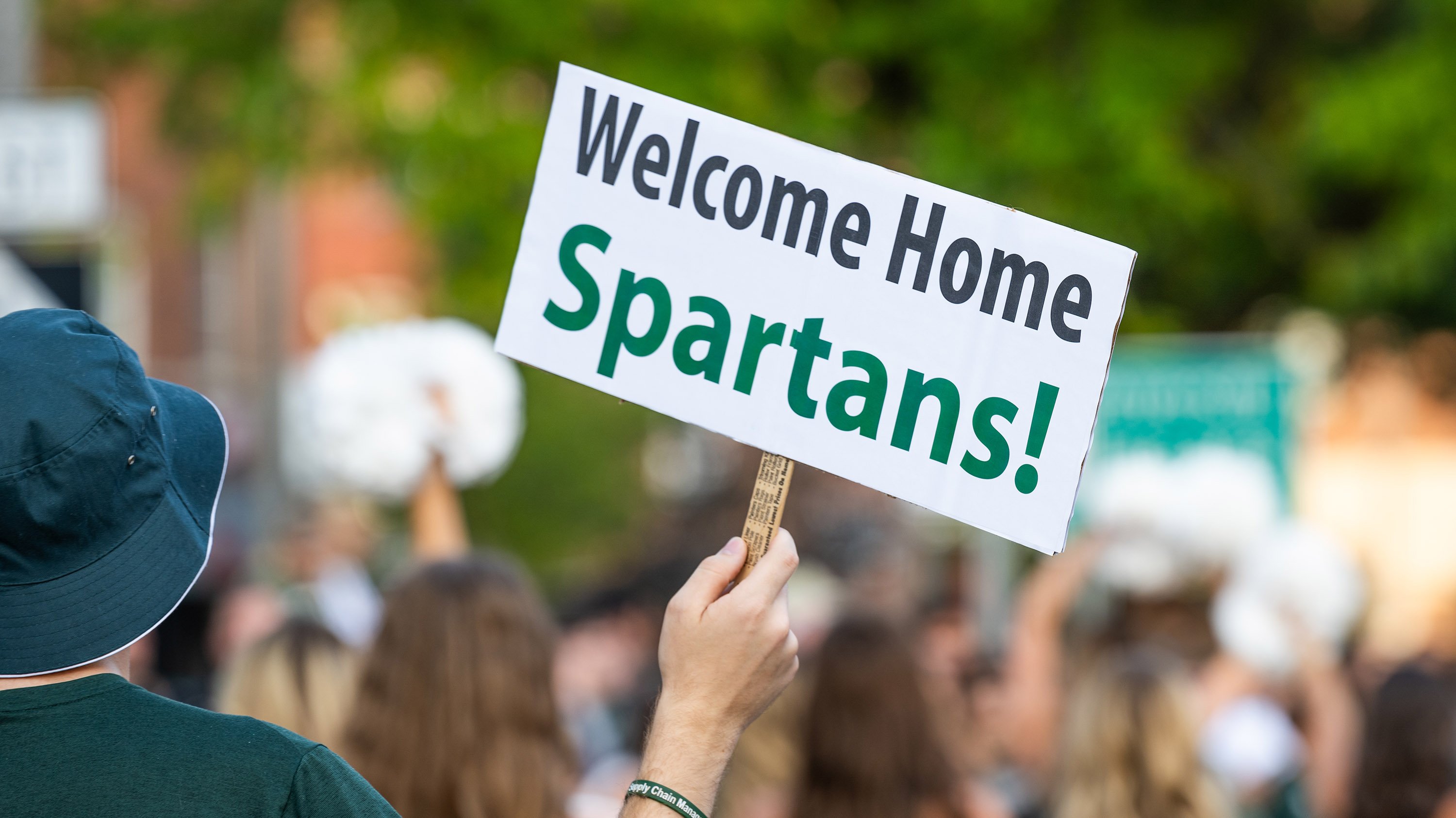 Hand holding sign that reads 'Welcome home Spartans!' at homecoming parade