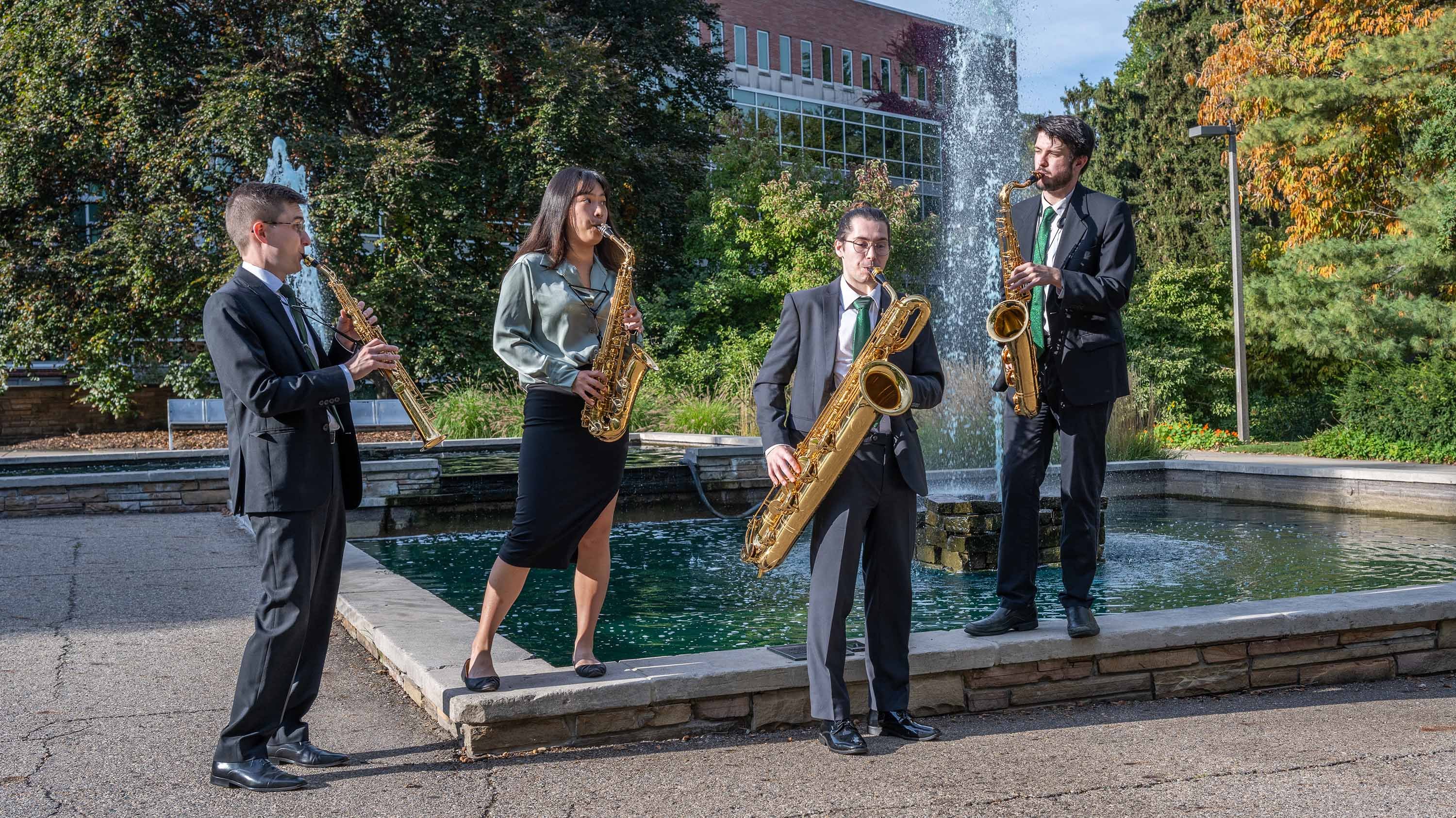 Four students playing instruments in front of library fountain