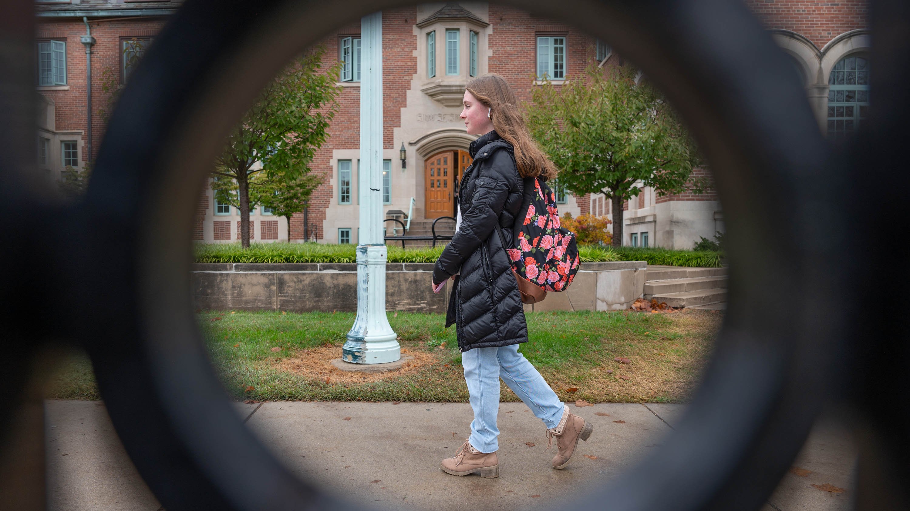 Student walking on campus, framed by a circular design in a fence's ironwork