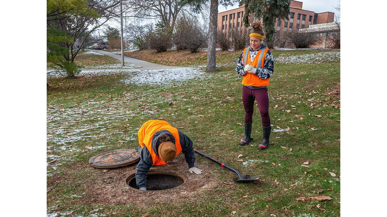 Students in orange vests testing waste water from manhole