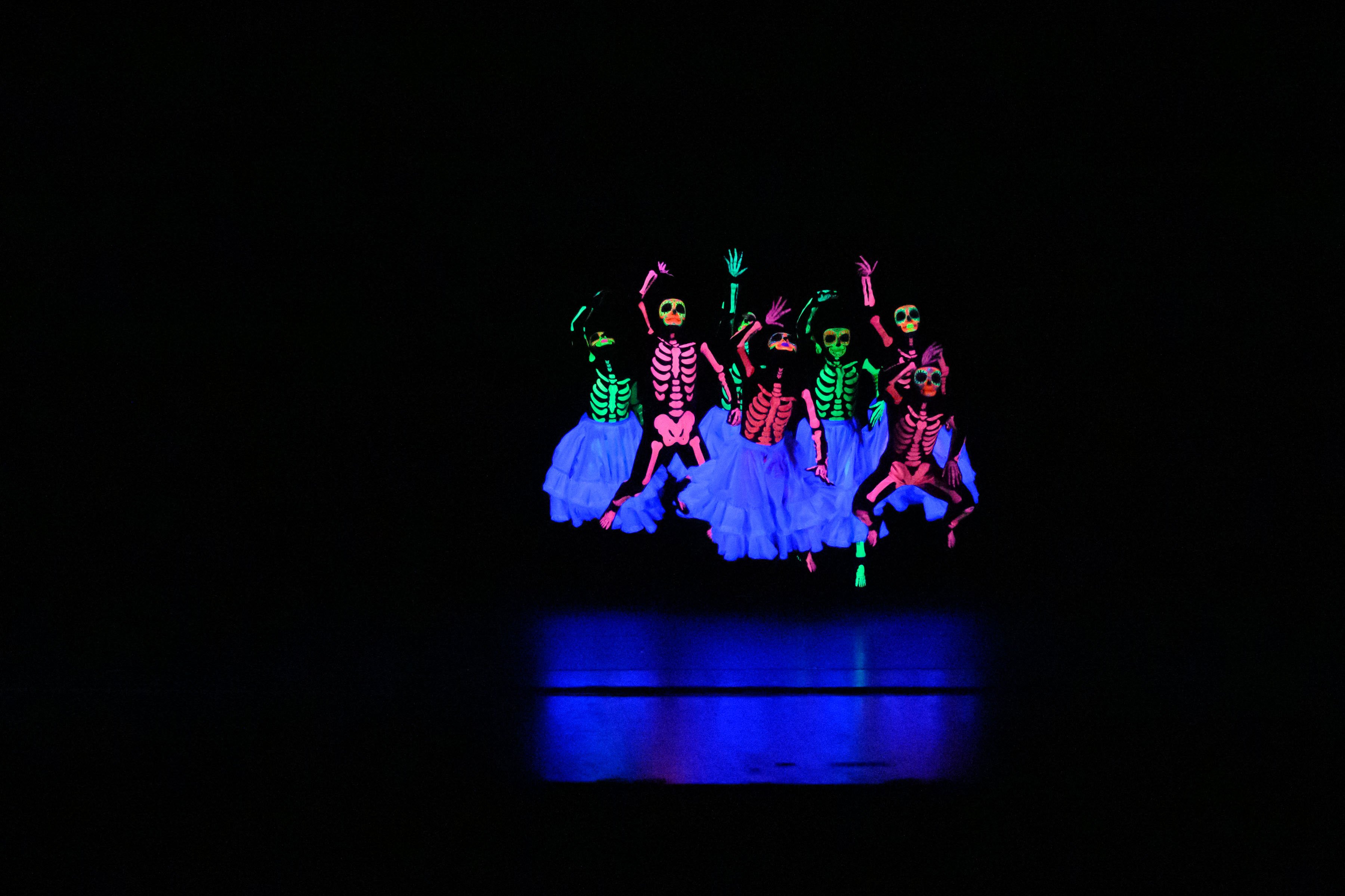 performers in skeleton and gown costumes leap up as a group