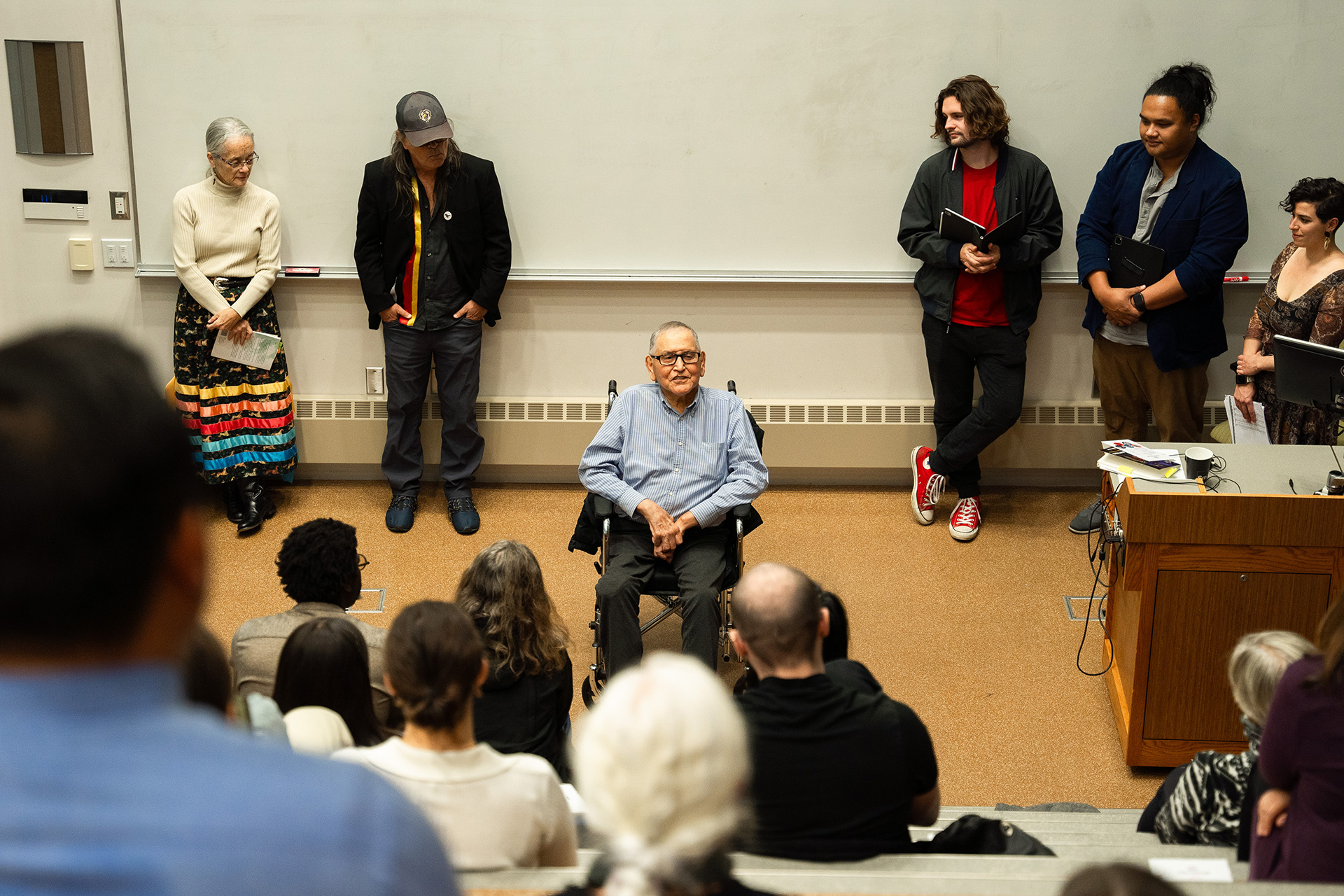 Glenn Wasicuna sits in front addressing the audience with additional speakers standing behind.